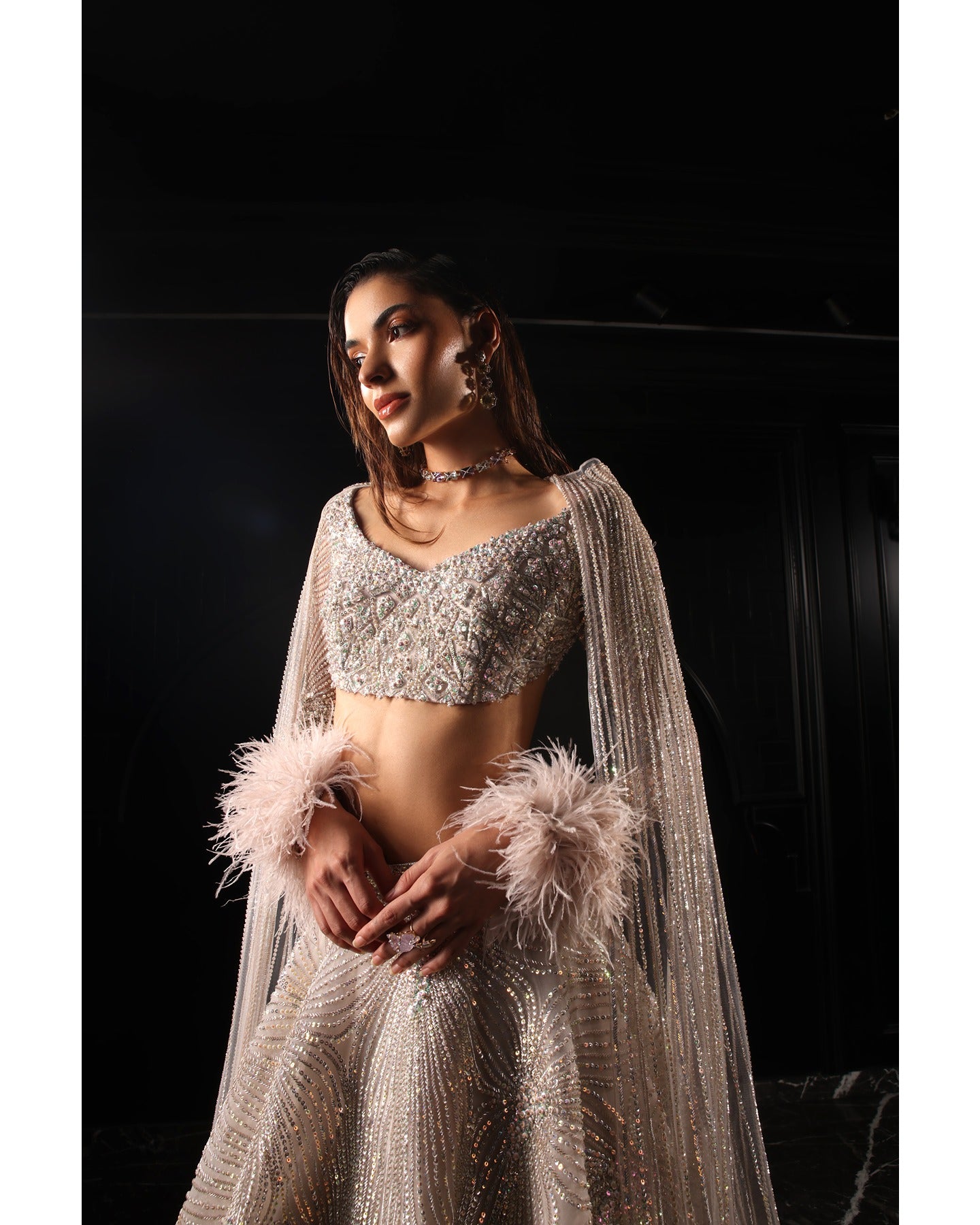 Drenched in lilac sophistication, the Orave lehenga captivates with its V-neck choli blouse and two shoulder trails embellished with Swarovski crystals, feathers, and sequins.