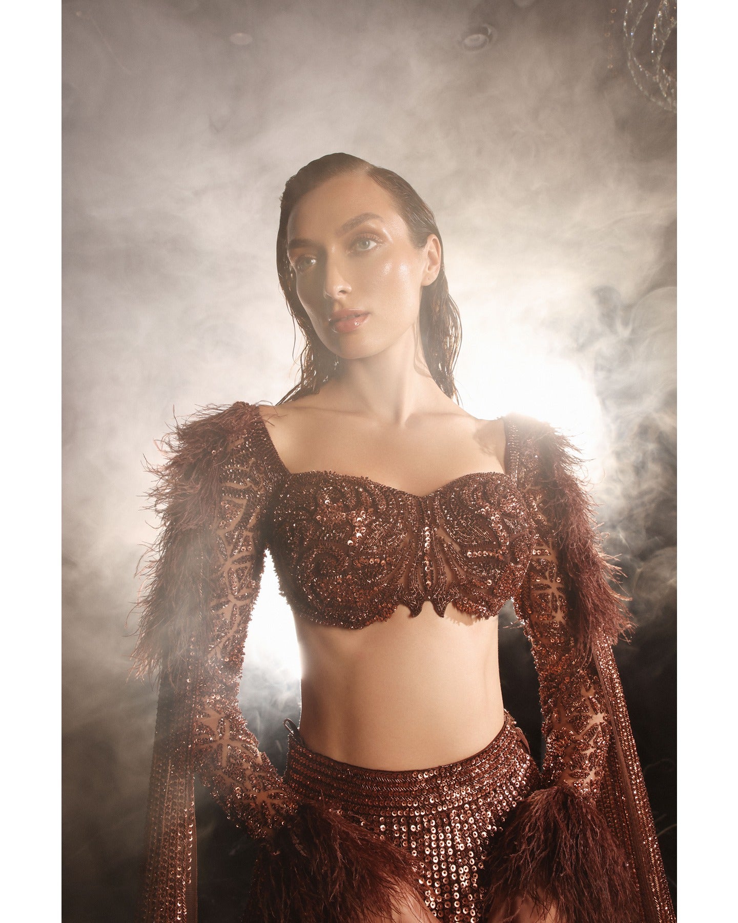Embrace the allure of the Orave lehenga with its choli cut blouse adorned in Swarovski crystals, feathers, and sequins, complemented by a captivating feather cape.