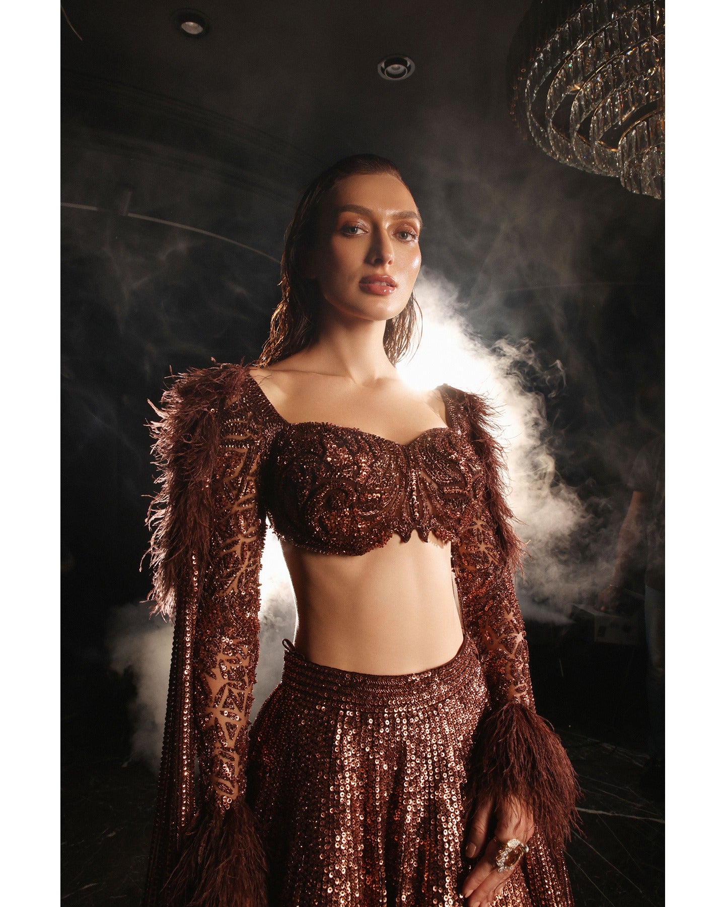 Embrace the allure of the Orave lehenga with its choli cut blouse adorned in Swarovski crystals, feathers, and sequins, complemented by a captivating feather cape.