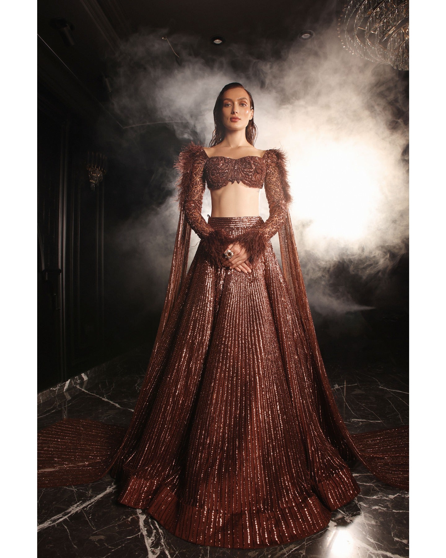 Embrace the allure of the Orave lehenga with its choli cut blouse adorned in Swarovski crystals, feathers, and sequins, complemented by a captivating feather cape.