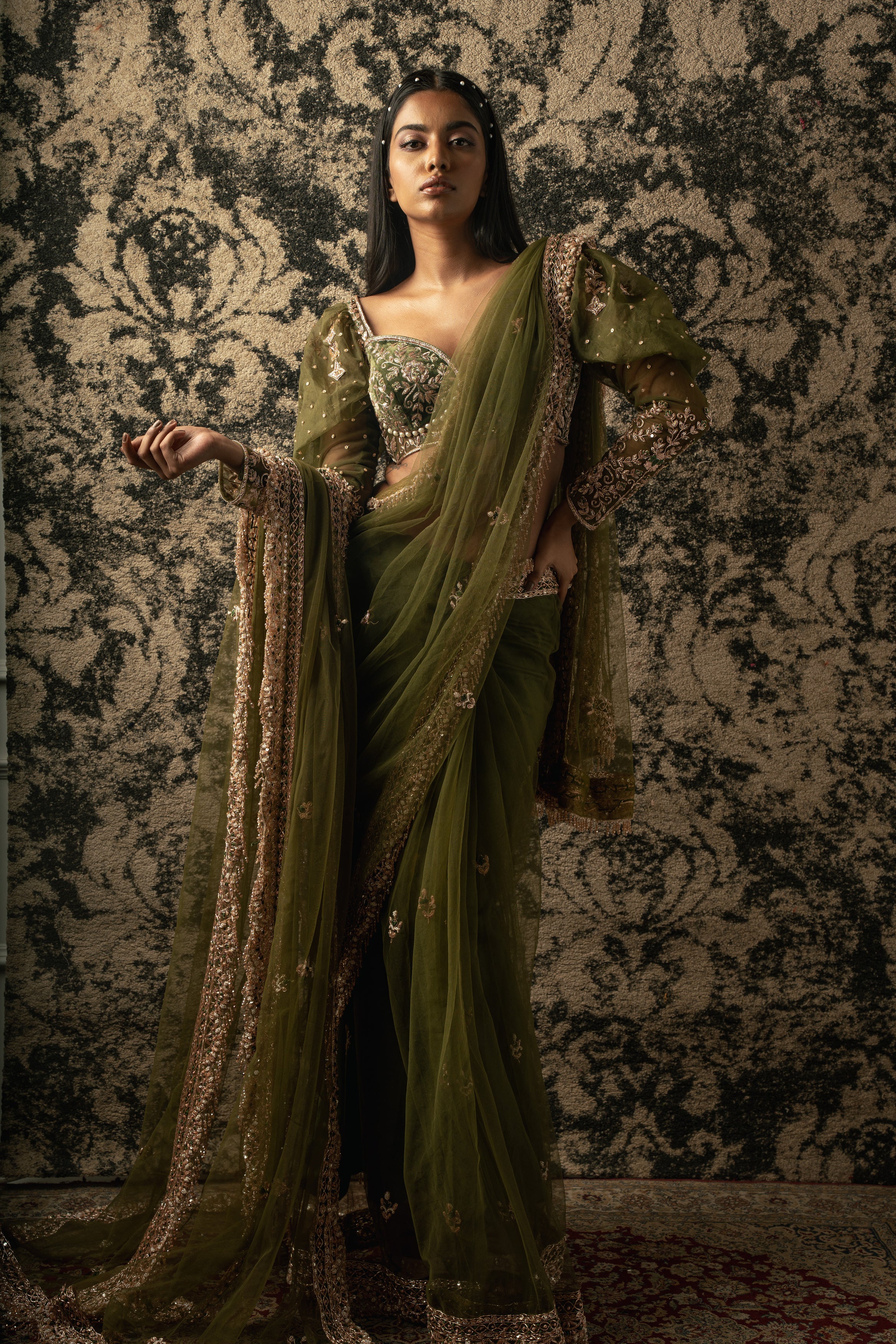 Drift into elegance with this ethereal Olive Green Net Saree, complemented by a luxurious Velvet and Organza blouse, a timeless ensemble for the modern woman.