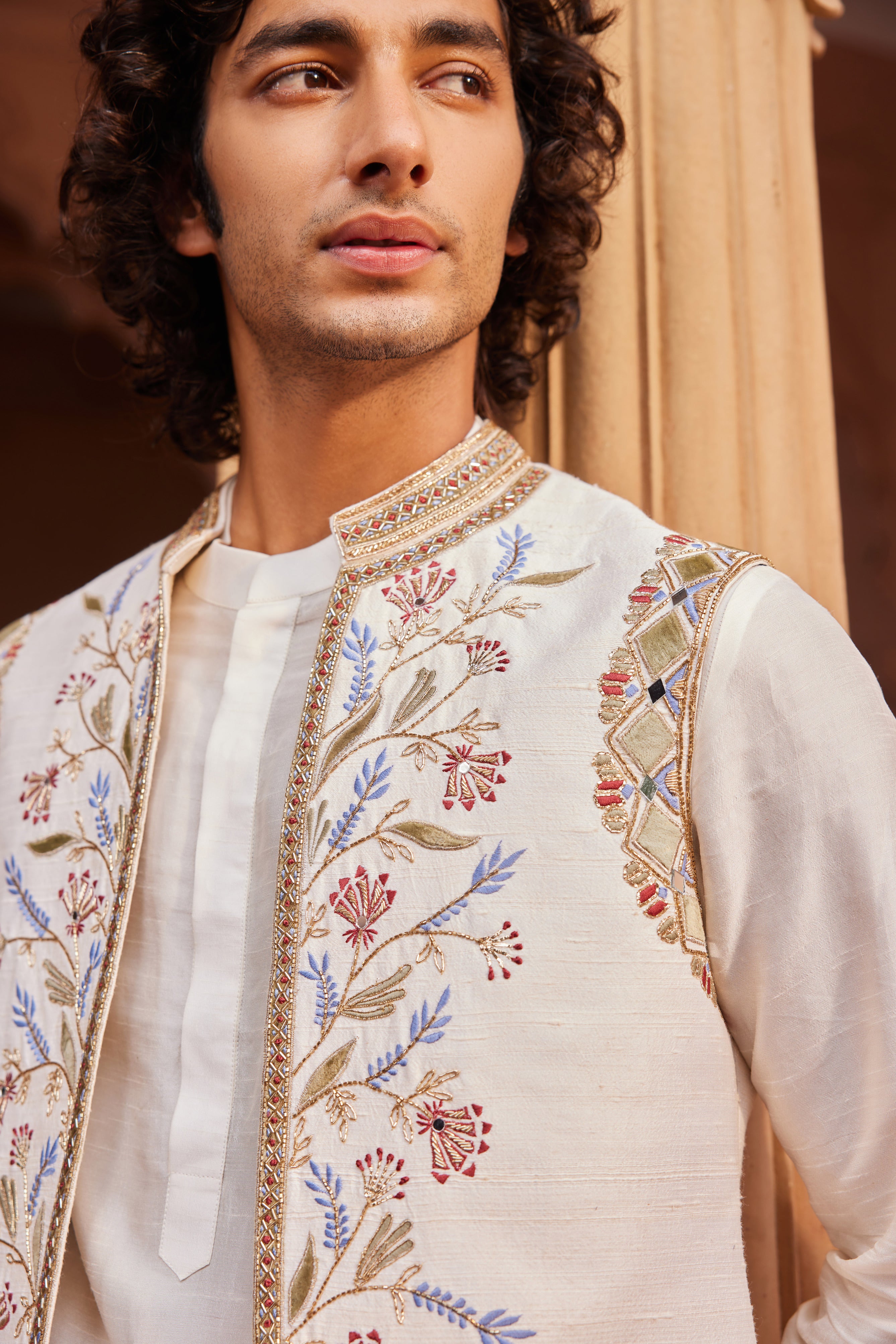 An ivory Nehru jacket adorned with a mix of colorful velvet applique techniques, zardozi, cutdana embroidery, and mirror embellishments. Paired with a finely detailed kurta and matching pants for a refined and elegant look.