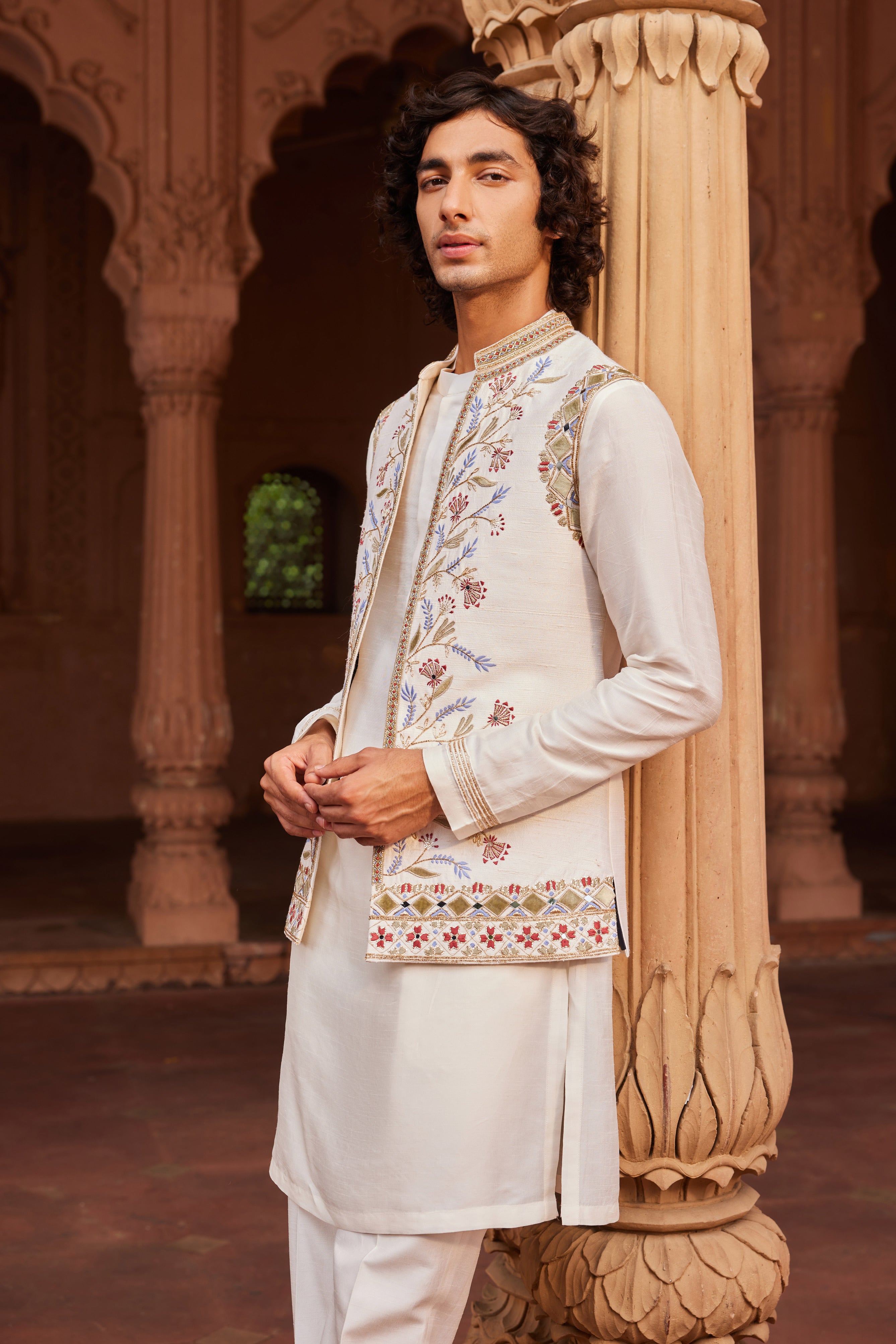 A luxurious ivory Nehru jacket featuring intricate velvet applique in vibrant colors, enhanced by zardozi, cutdana work, and shimmering mirror embellishments. Paired with a beautifully detailed kurta and pants, this set offers a perfect blend of rich texture and intricate handwork for a striking, sophisticated ensemble.