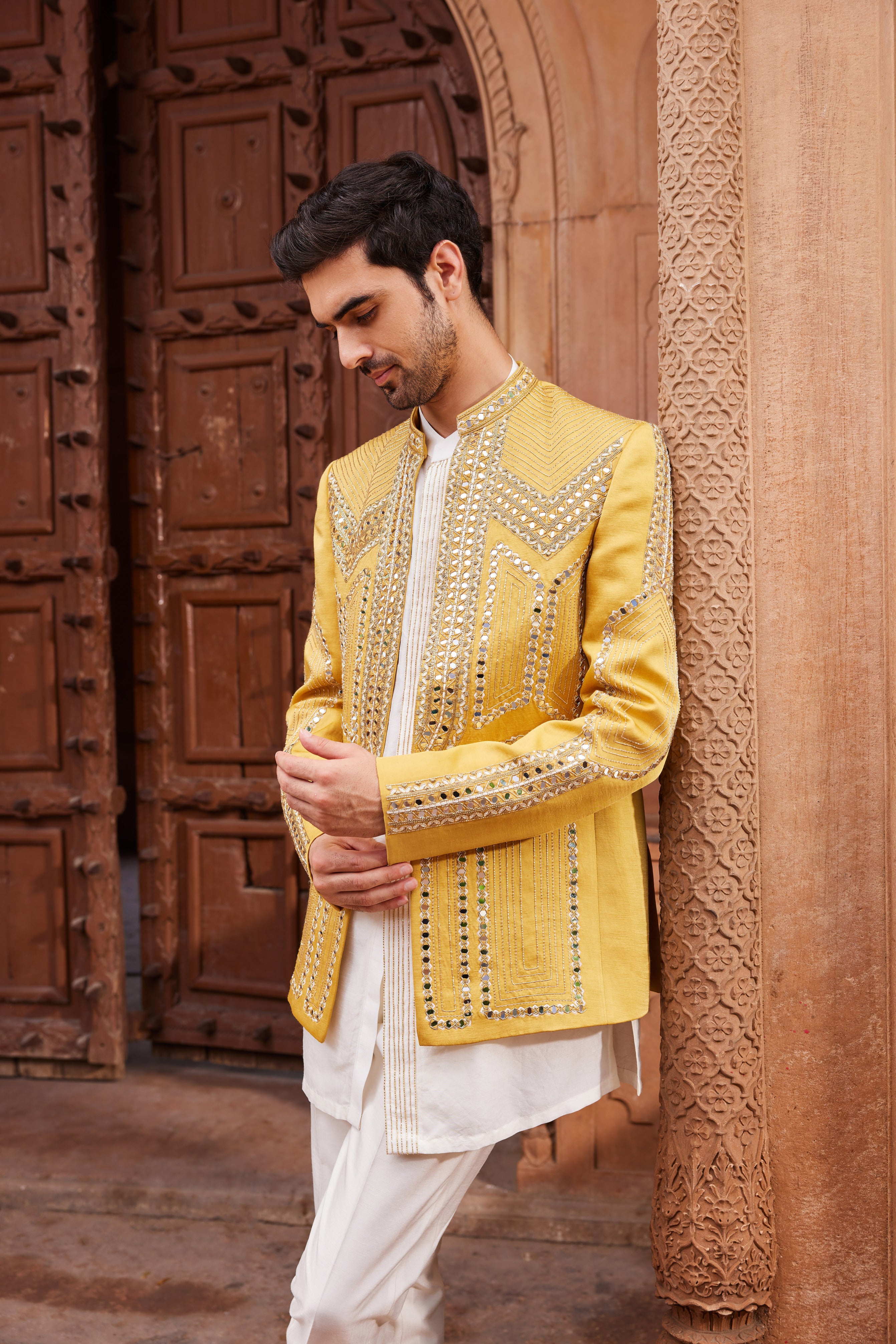 Full view of a geometric patterned jacket richly embellished with mirrors and resham zardozi embroidery, paired with a statement front-open kurta and tailored pants for a striking ensemble.