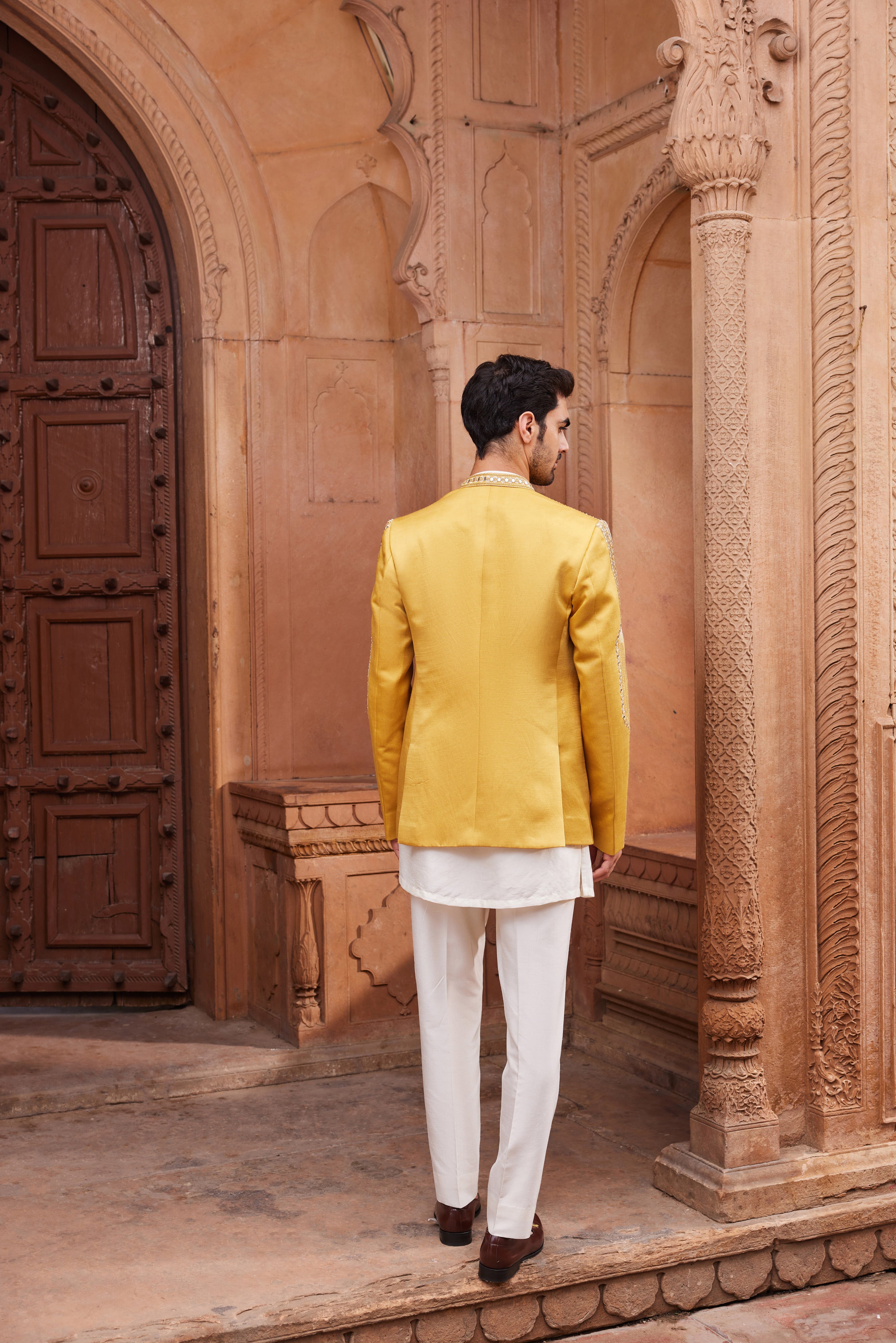 Full view of a geometric patterned jacket richly embellished with mirrors and resham zardozi embroidery, paired with a statement front-open kurta and tailored pants for a striking ensemble.