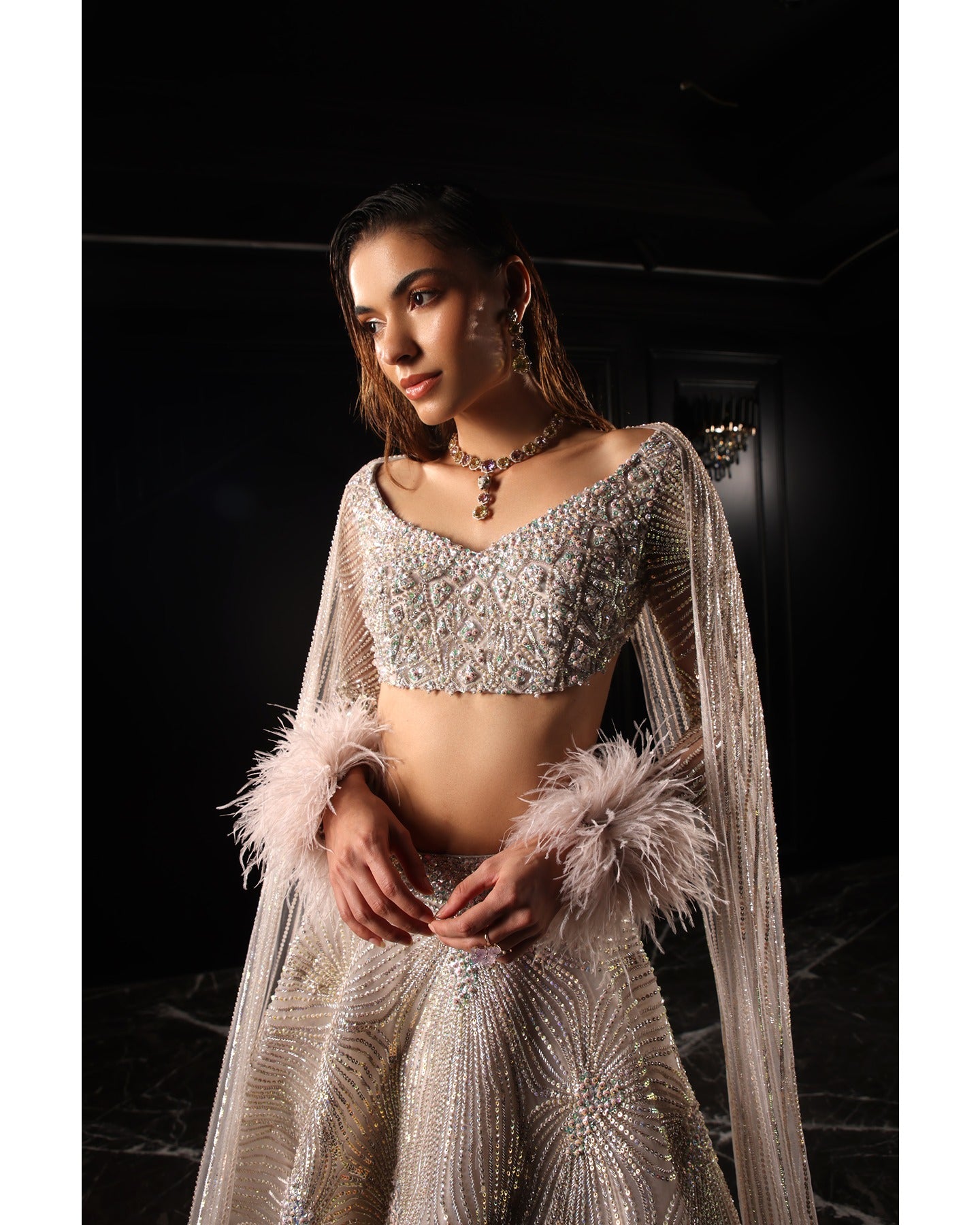 Drenched in lilac sophistication, the Orave lehenga captivates with its V-neck choli blouse and two shoulder trails embellished with Swarovski crystals, feathers, and sequins.