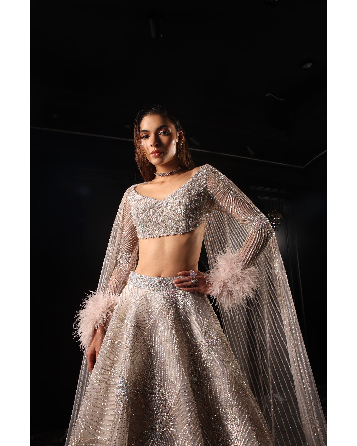 Drenched in lilac sophistication, the Orave lehenga captivates with its V-neck choli blouse and two shoulder trails embellished with Swarovski crystals, feathers, and sequins.