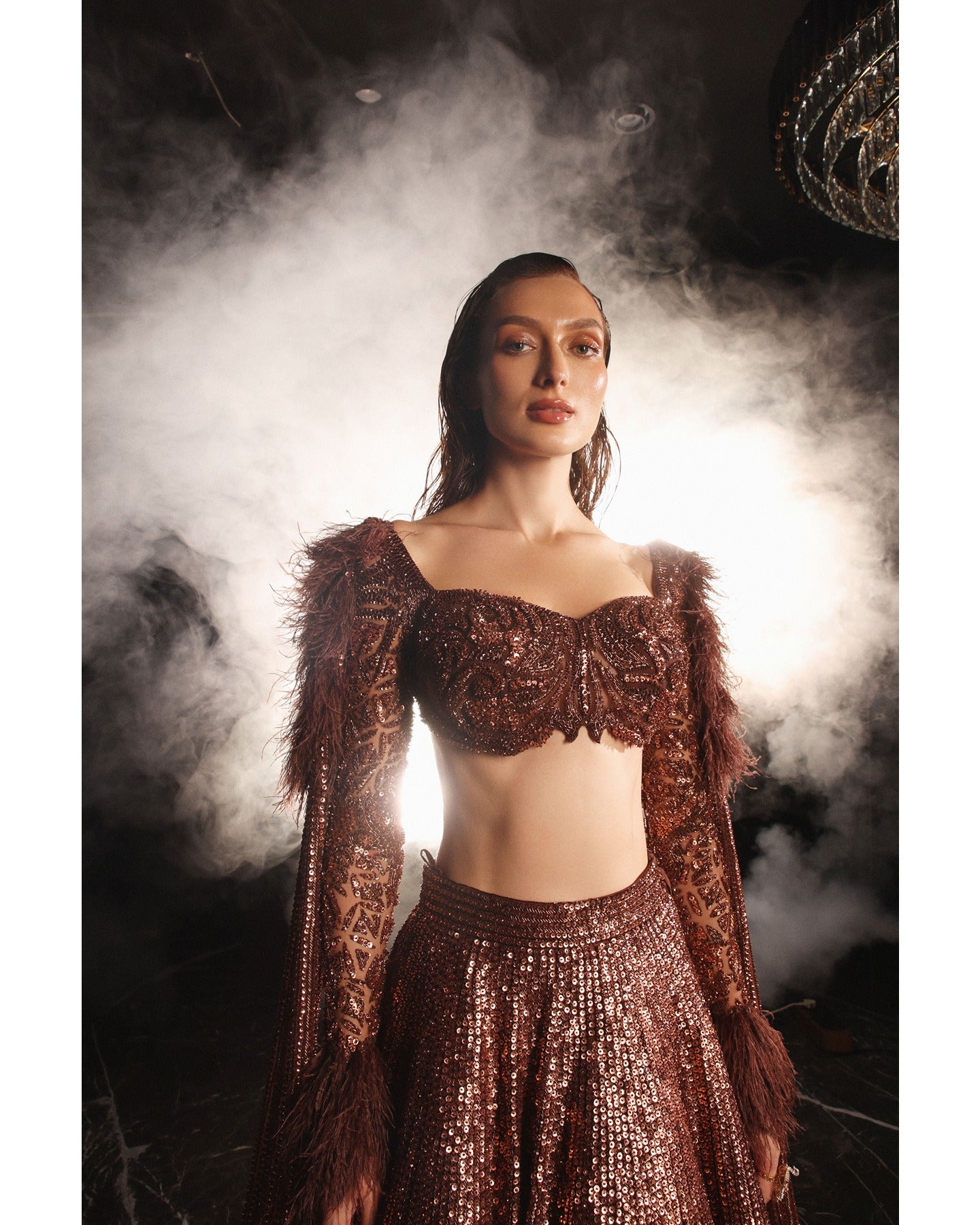 Embrace the allure of the Orave lehenga with its choli cut blouse adorned in Swarovski crystals, feathers, and sequins, complemented by a captivating feather cape.
