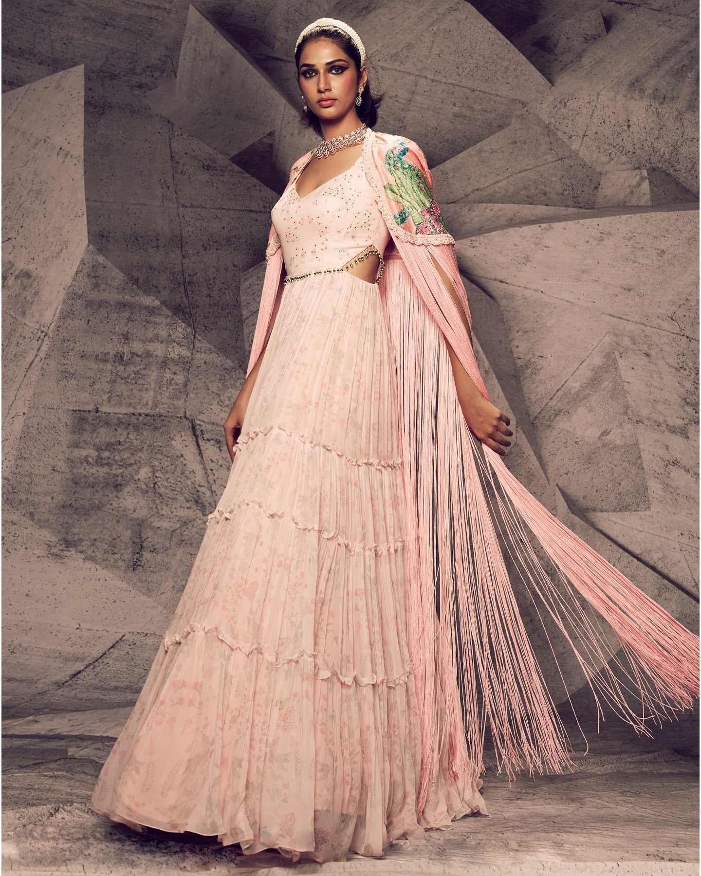 Radiating in the soft hues of pink, this georgette anarkali with delicate tassels and a statement fringe cape is a vision of feminine grace and timeless beauty.
