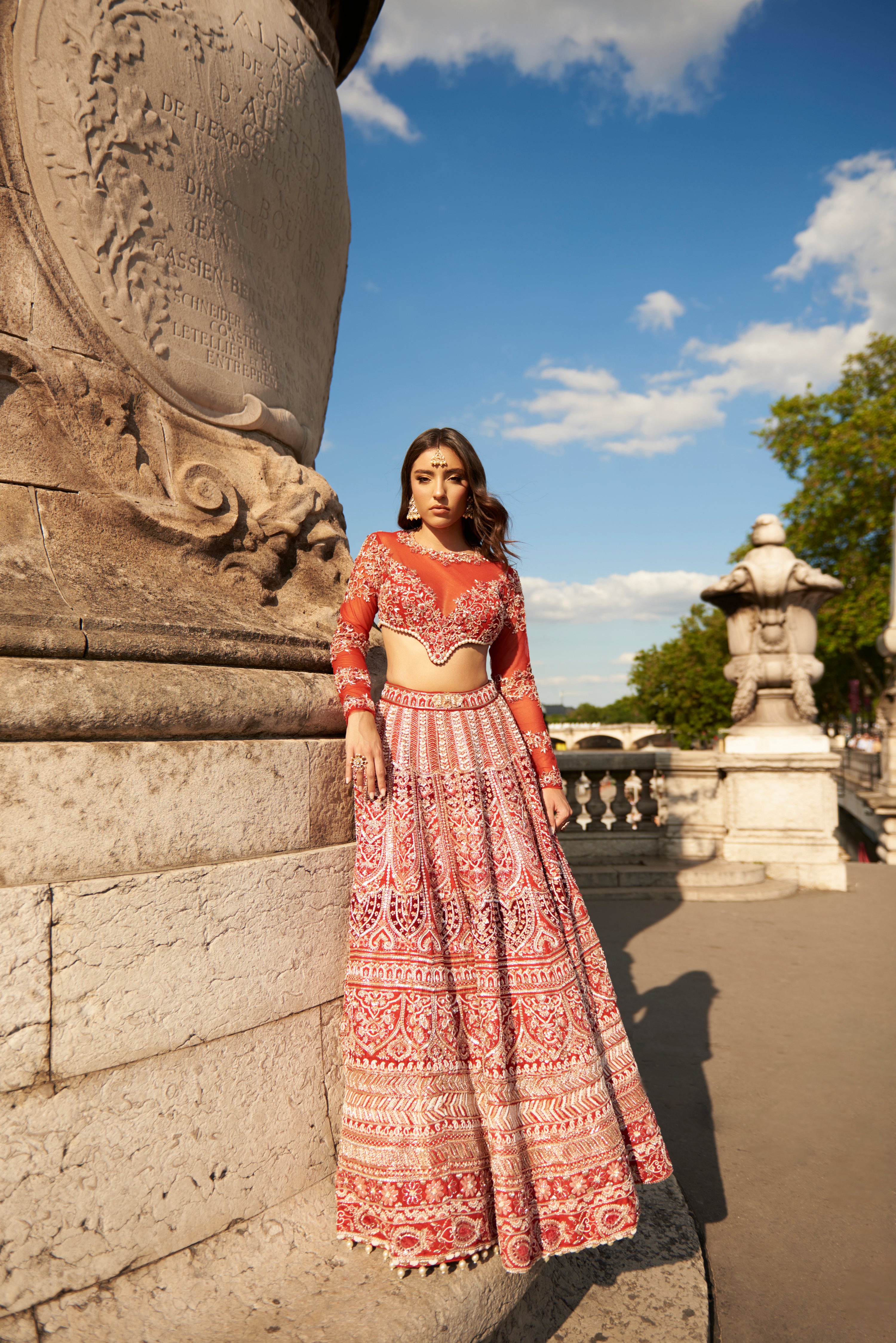 Full-sleeve red lehenga set in carnelian red, featuring intricate hand embroidery and pearl embellishments, crafted from luxurious raw silk and velvet, paired with a sheer net full-sleeve blouse and dupatta