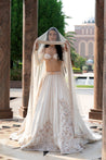 Elegant white lehenga in linen satin with gold-accented Chikankari handwork, paired with a pearl-embellished blouse and a flowing net dupatta.