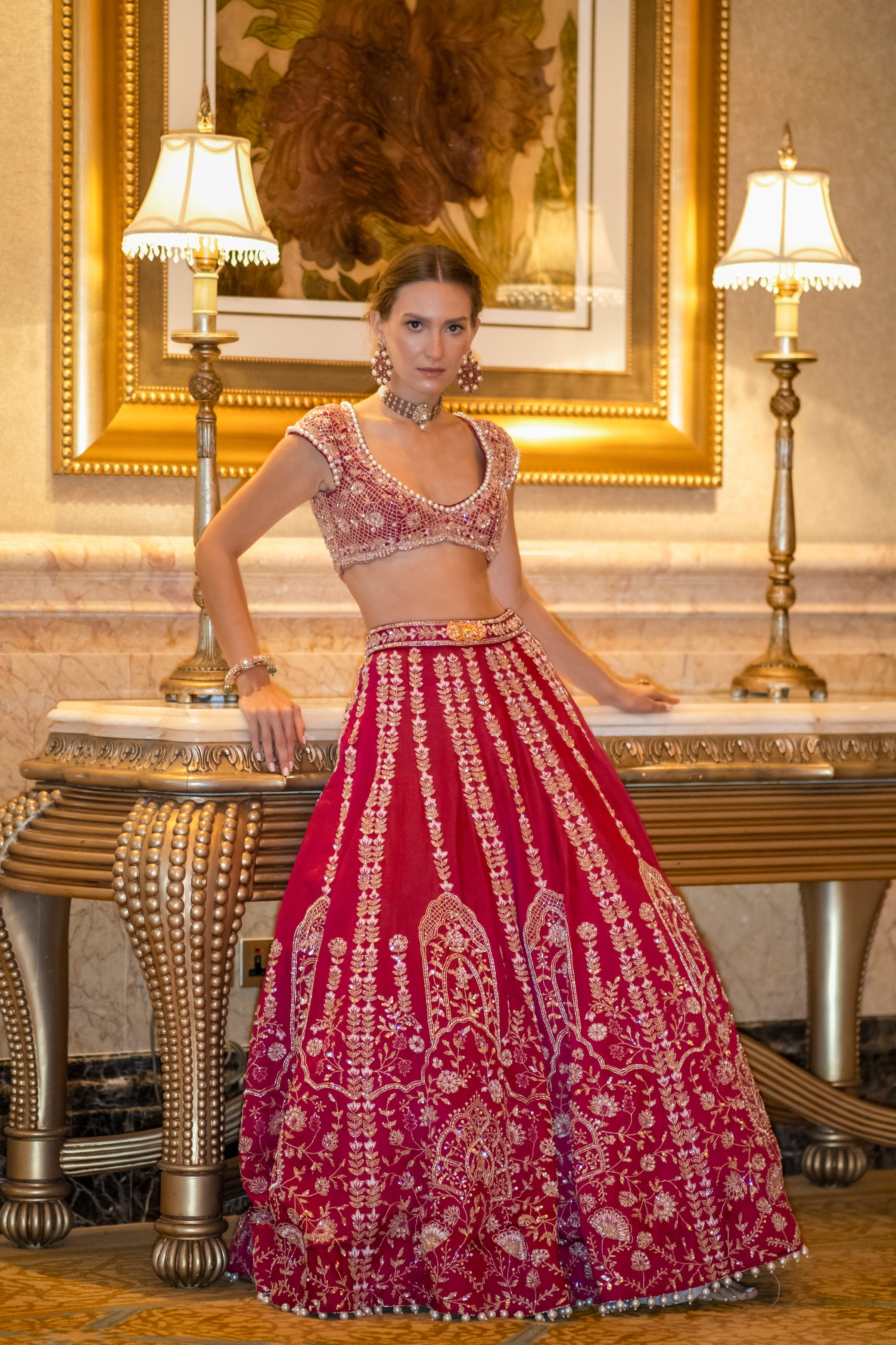 Luxurious carmine red lehenga in Habutai silk with detailed cutdana work and pearl accents, paired with a cap-sleeved blouse showcasing floral and rhombus motifs