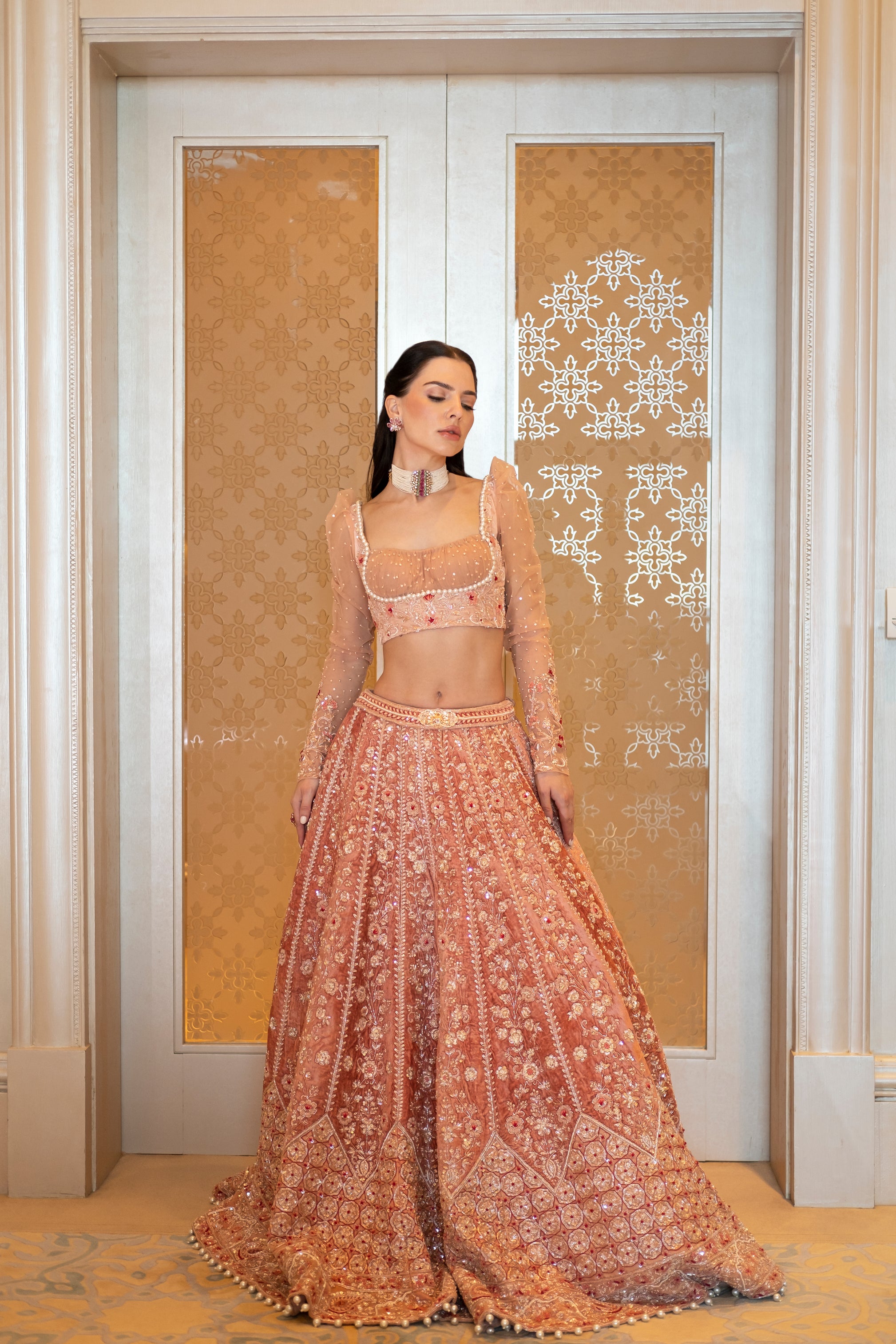 Soft peach velvet lehenga with intricate handwork, paired with a puff-sleeve blouse and a net dupatta with embroidered borders