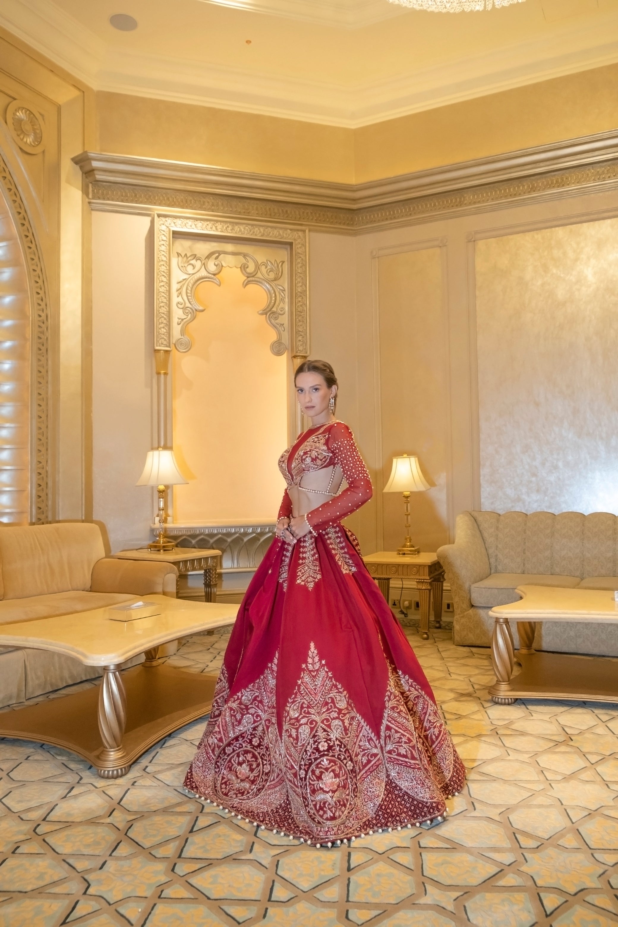 Rich red lehenga with gold zardoshi handwork and maroon velvet accents, featuring a pearl-strapped blouse and embroidered net dupatta.