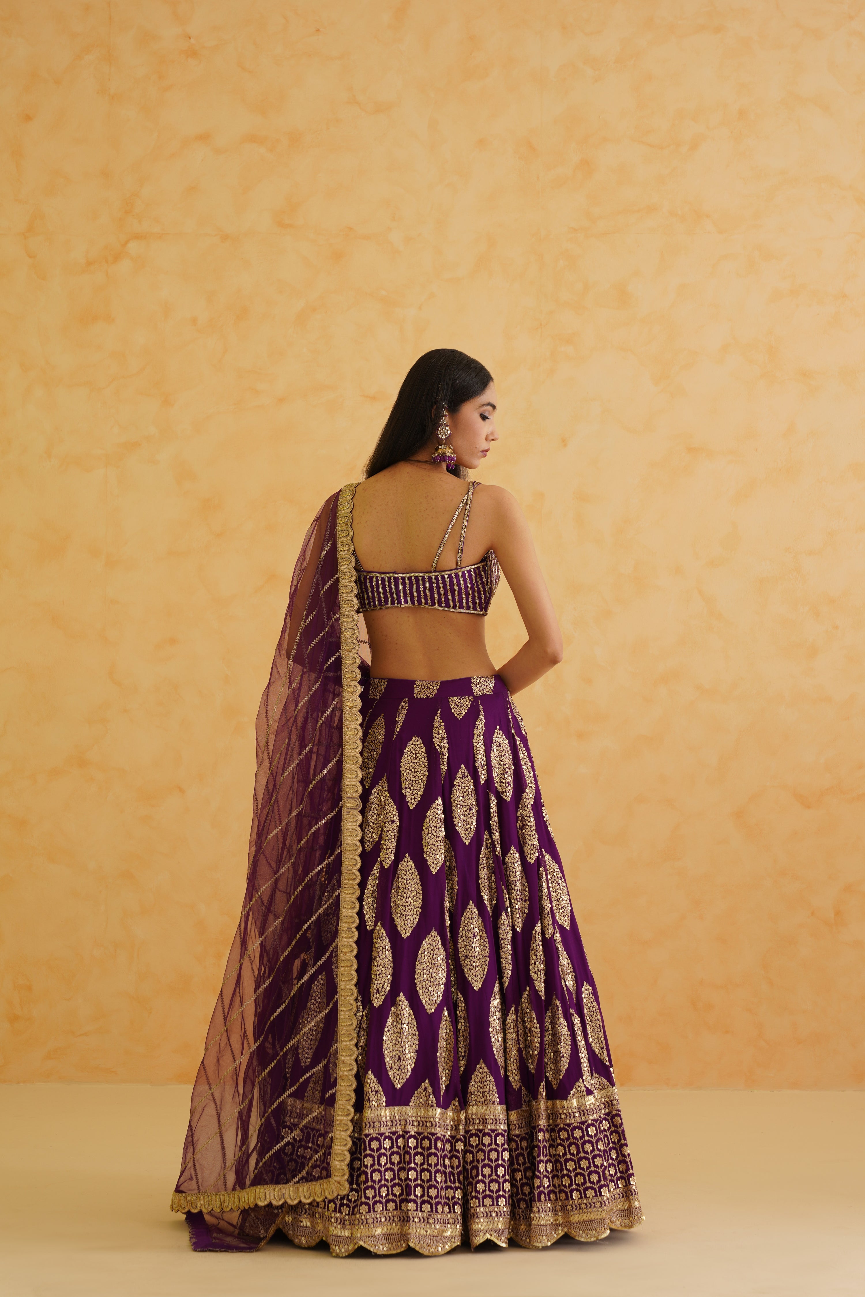 Intricate embroidery on the blouse includes shimmering crystals and stones, enhancing the overall elegance of the purple lehenga.