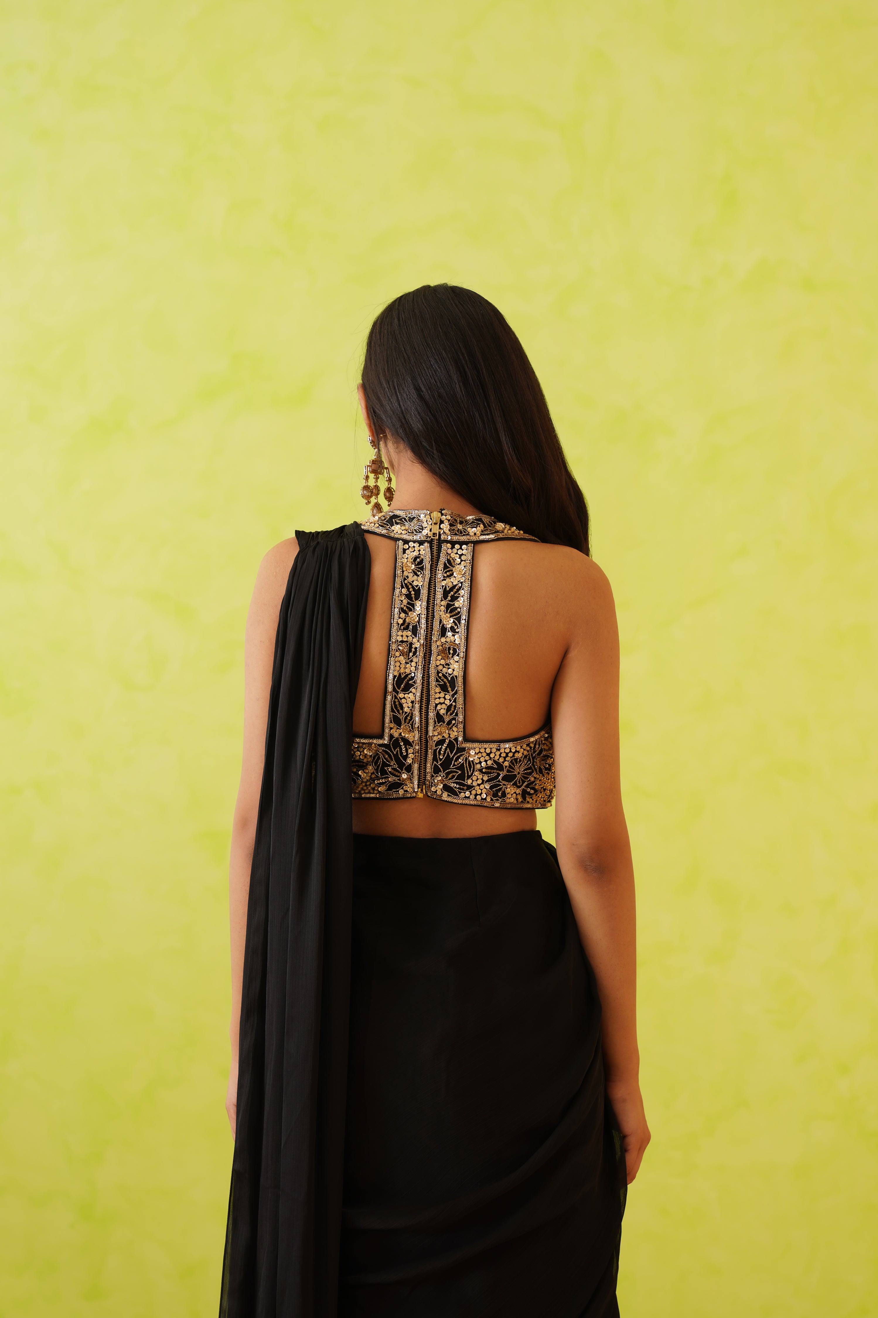 Sophisticated black saree with a modern drape, complemented by an intricately detailed blouse adorned with gold sequins, stones, and pearl embellishments.