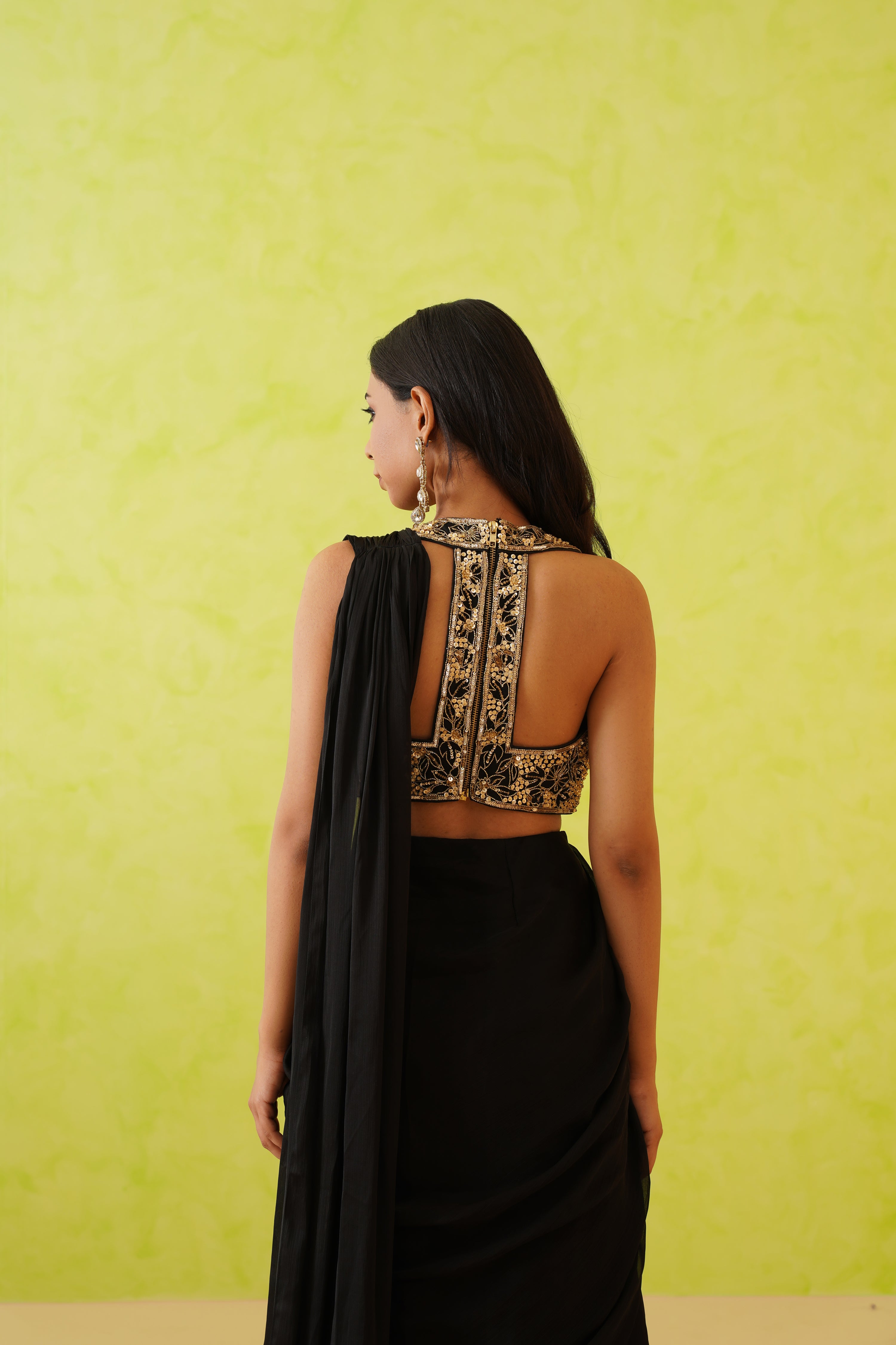 Chic black draped saree showcasing a full-length design, paired with a glamorous blouse embellished with floral motifs in gold and pearl accents.