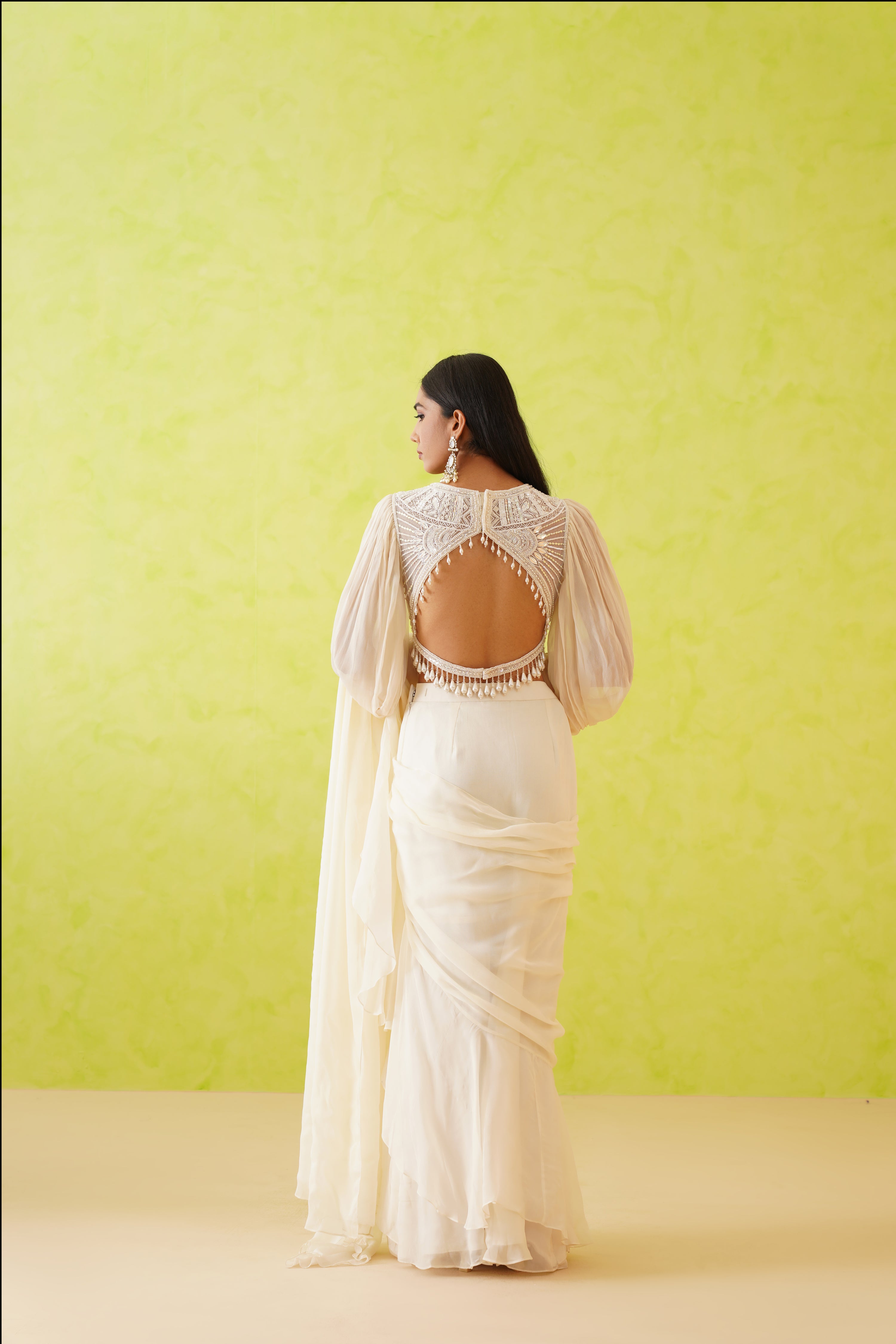 Sophisticated white saree showcasing a modern drape, complemented by a stunning blouse adorned with intricate white sequin and pearl embellishments.