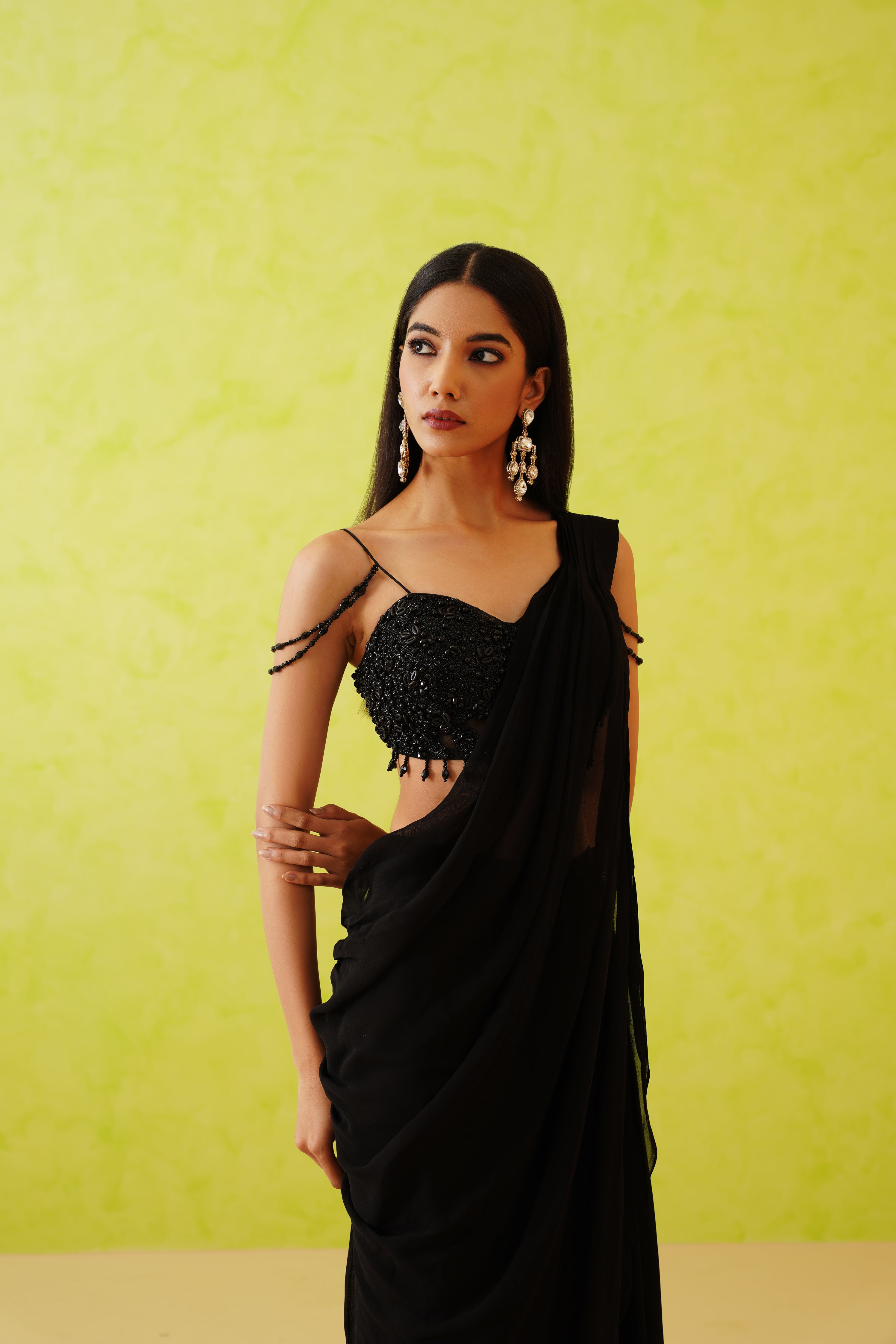 Chic black draped saree with a graceful flow, enhanced by a glamorous blouse featuring intricate embellishments of black sequins, stones, and crystal floral patterns.