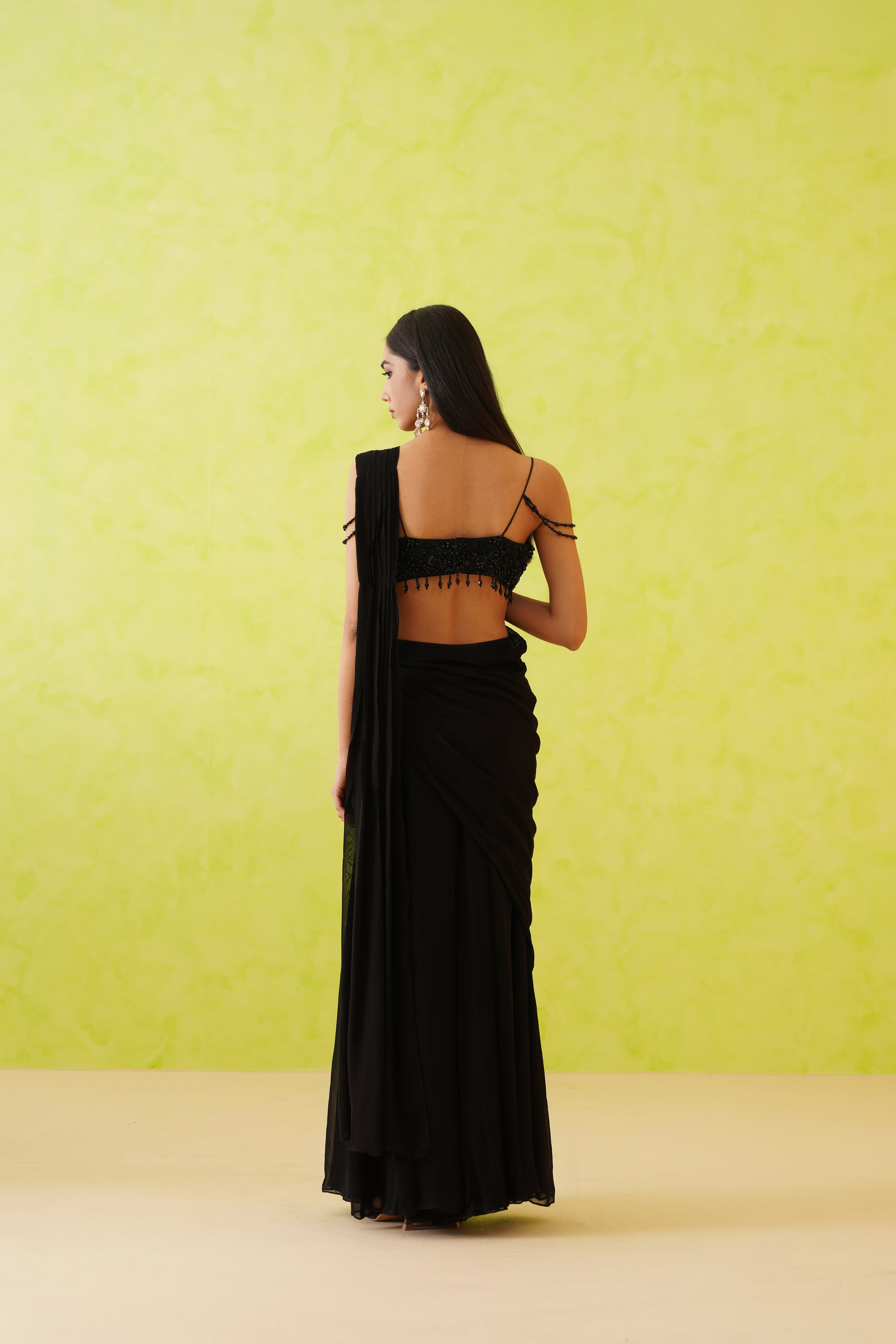 Sophisticated black saree with a contemporary drape, paired with a blouse richly detailed in black tonal sequins and pearls, creating a stunning floral motif.