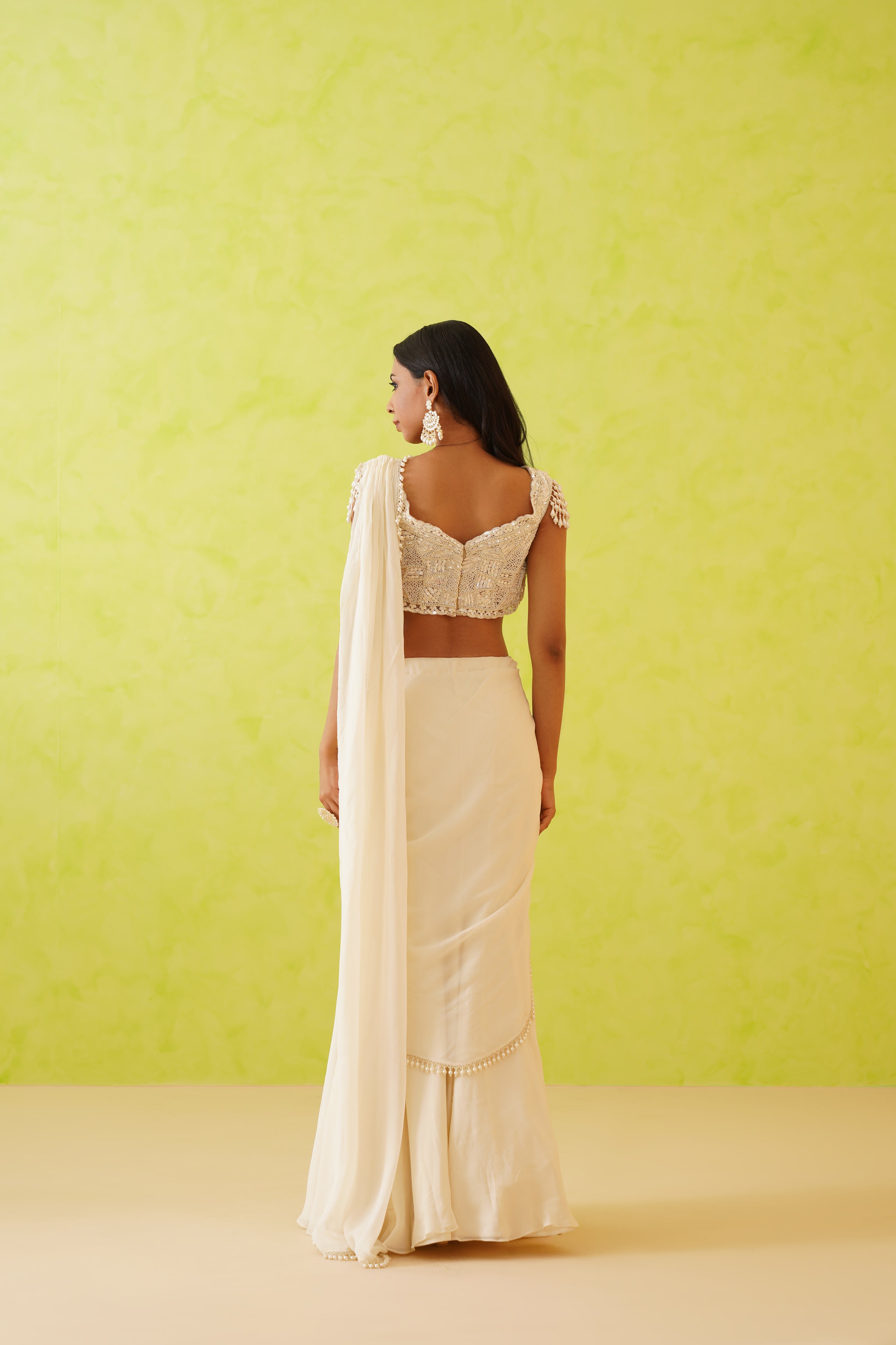 White modern draped saree with a flowy silhouette, complemented by an embellished blouse decorated with sequins, stones, and pearls in floral motifs.