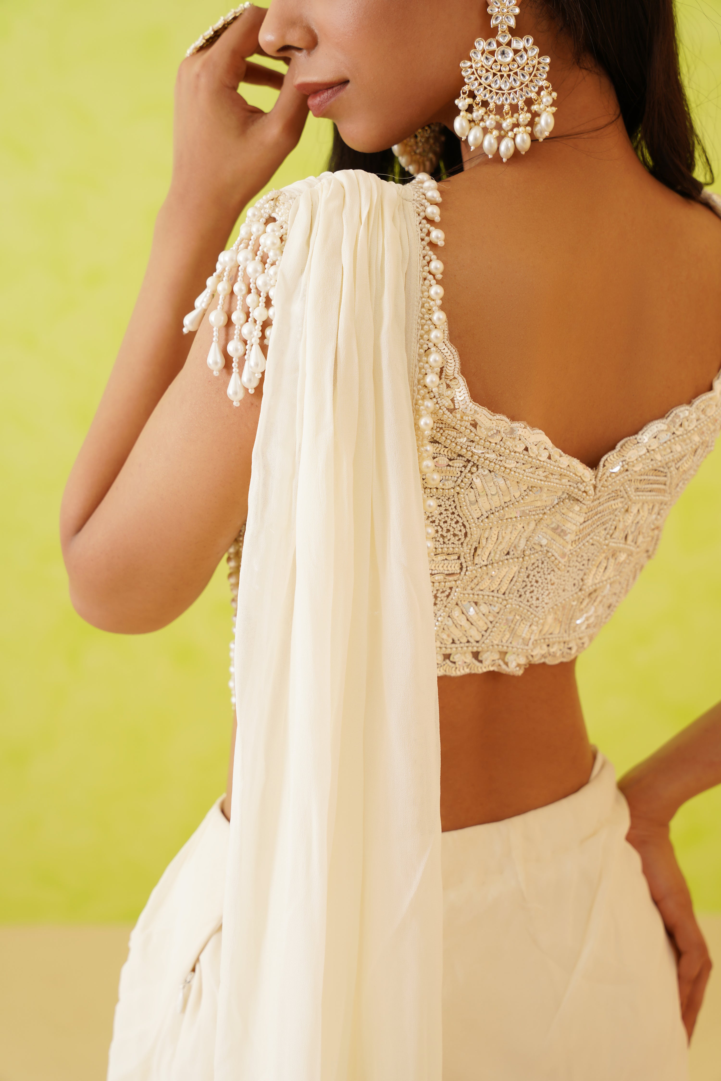 Stunning white saree with a full-length drape, paired with a blouse adorned with intricate sequins, crystals, and pearl embellishments in floral patterns.