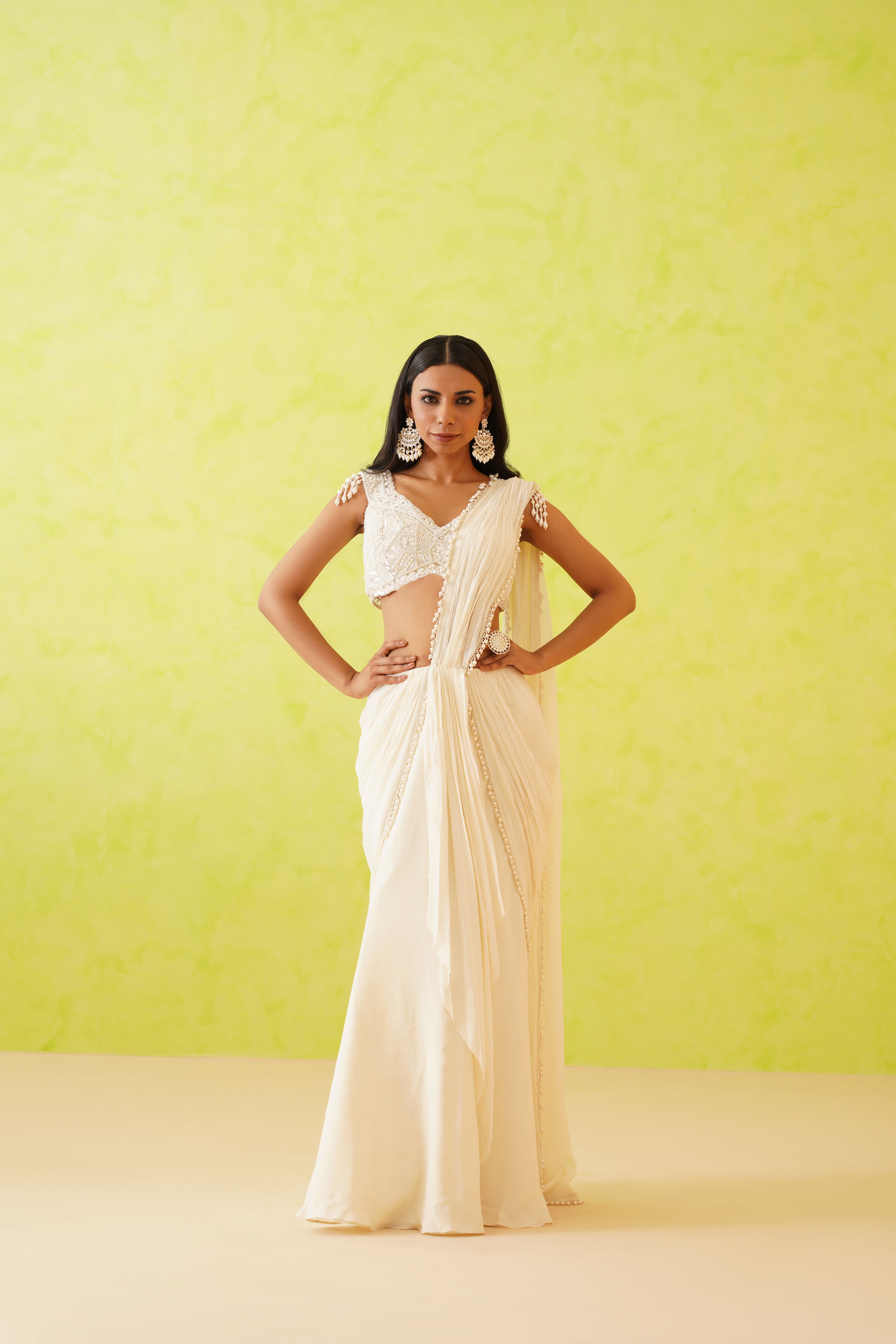 Graceful white saree with a sleek drape, paired with a floral-patterned blouse featuring white sequins, crystals, and pearl accents.