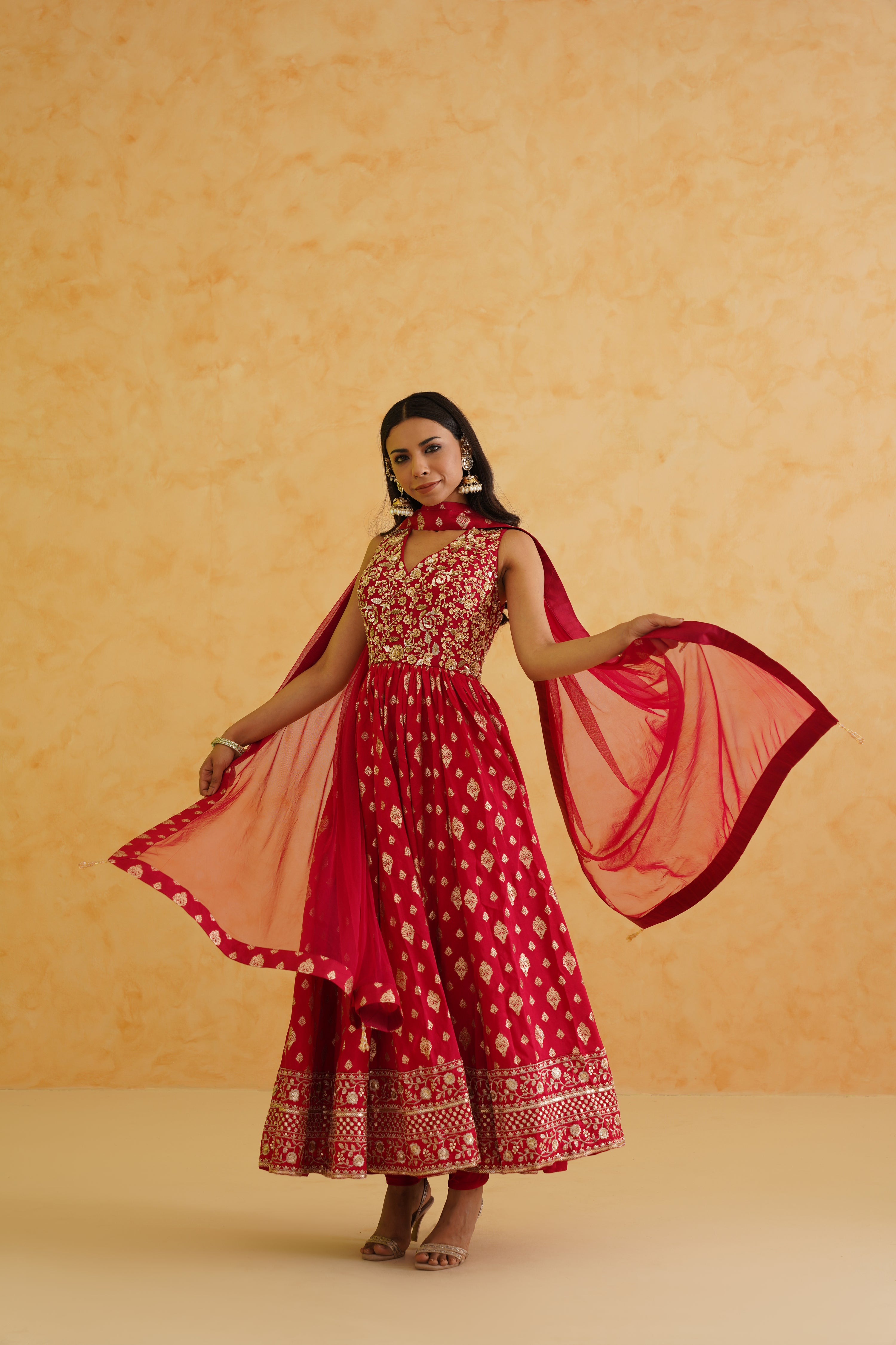 A luxurious red anarkali ensemble featuring a flowing silhouette and a matching net dupatta, ideal for weddings and parties.