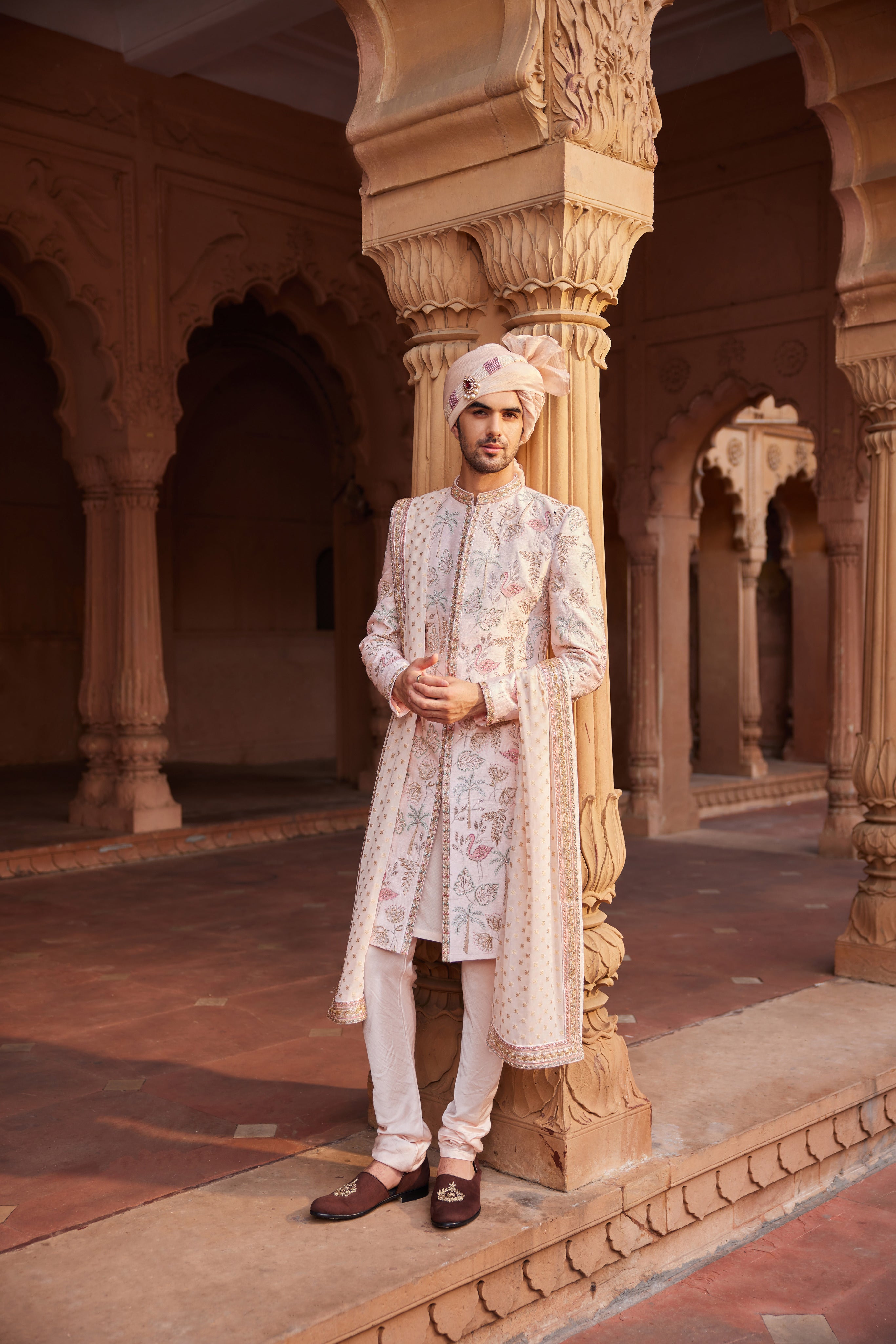 A sherwani intricately designed with a stunning mix of colorful resham, zari, zardozi, and dabka work, showcasing a variety of unique motifs. It is paired with a matching kurta and pant set, along with an embroidered stole draped over the shoulder.