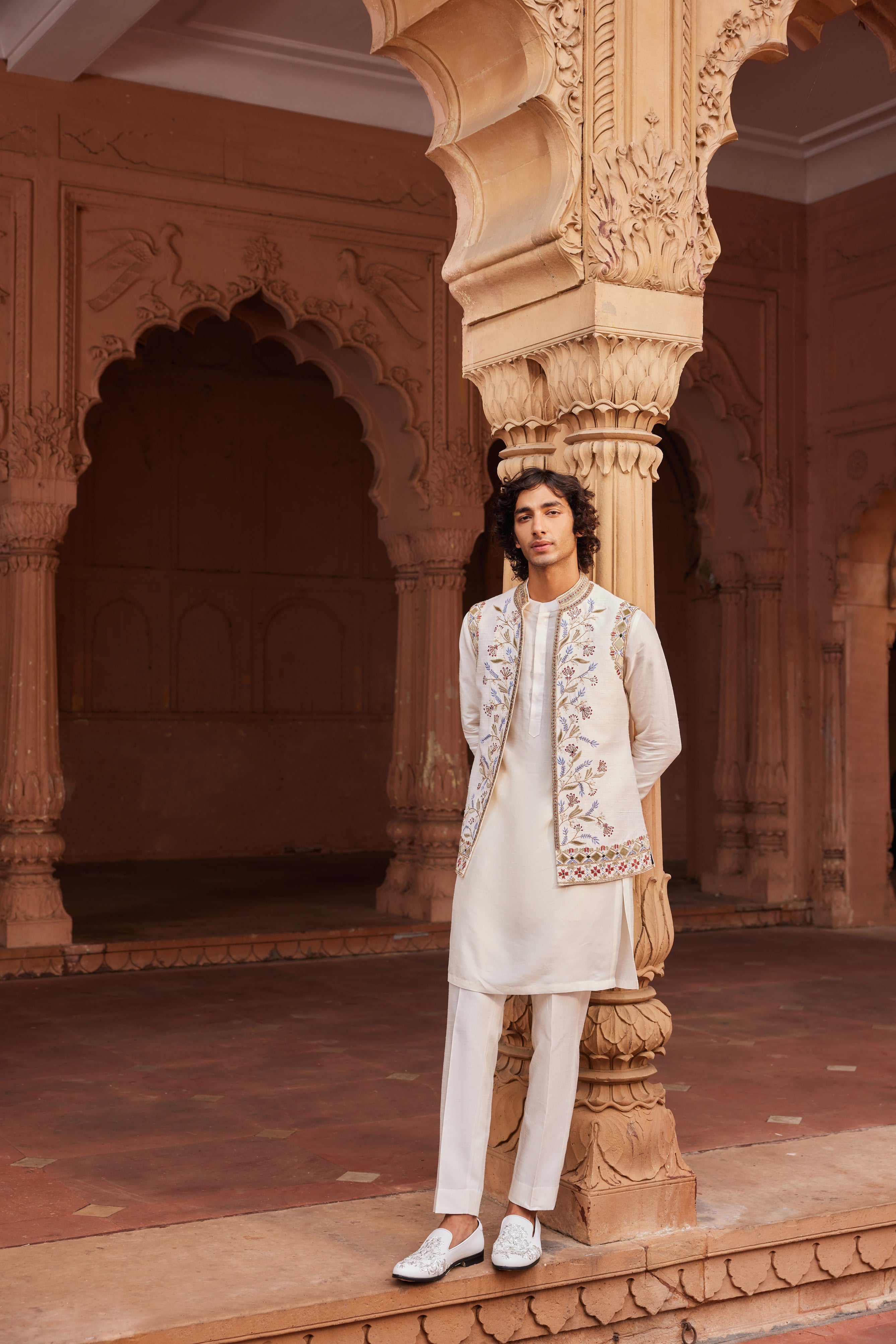 An ivory Nehru jacket featuring colorful velvet applique, zardozi, cutdana work, and mirror embellishments, paired with a detailed kurta and pants.