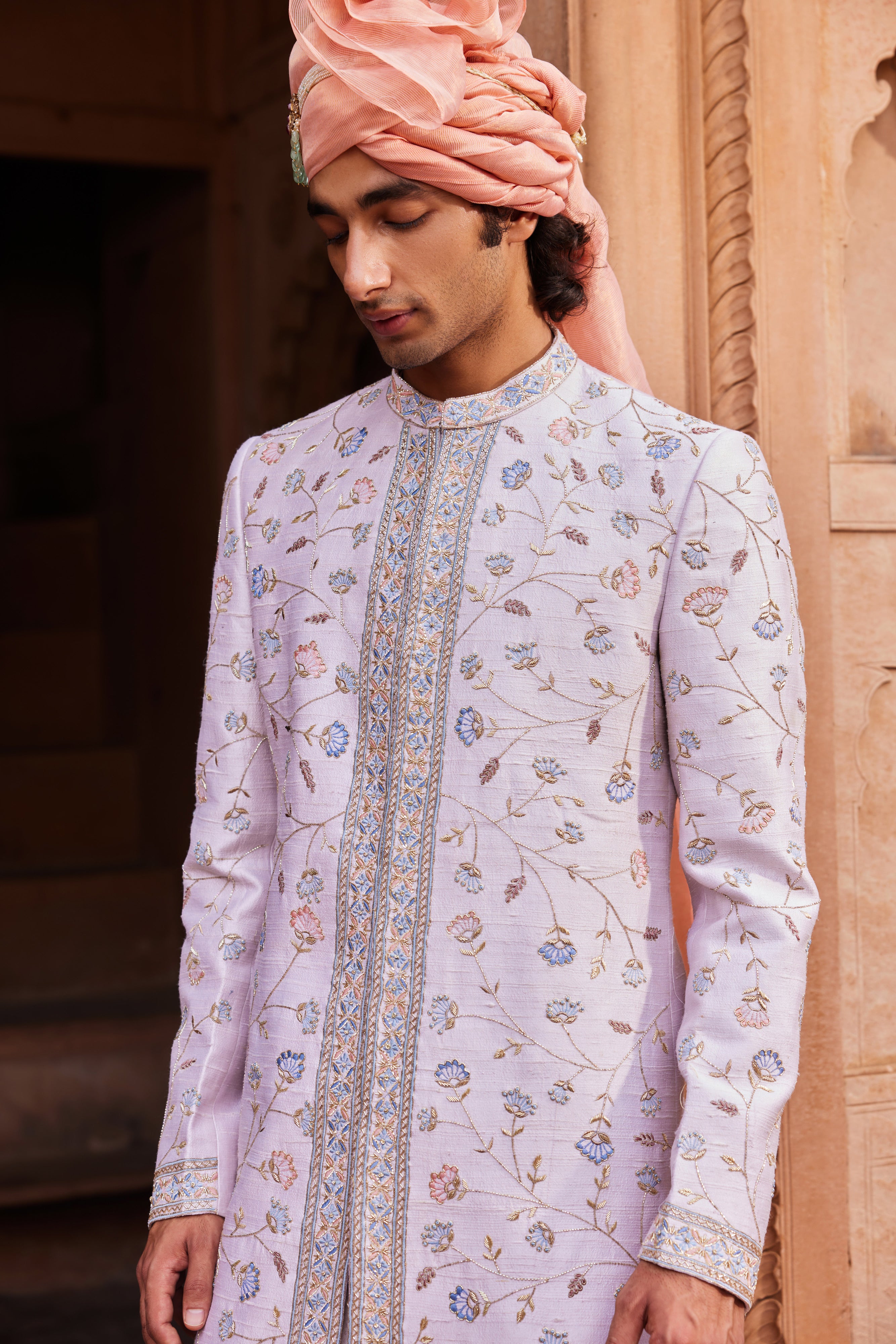 A sherwani adorned with a delicate mix of colorful resham, zari, zardozi, and dabka work, featuring a beautiful blend of floral and symmetrical patterns. It is paired with a kurta, pants, and an embroidered stole