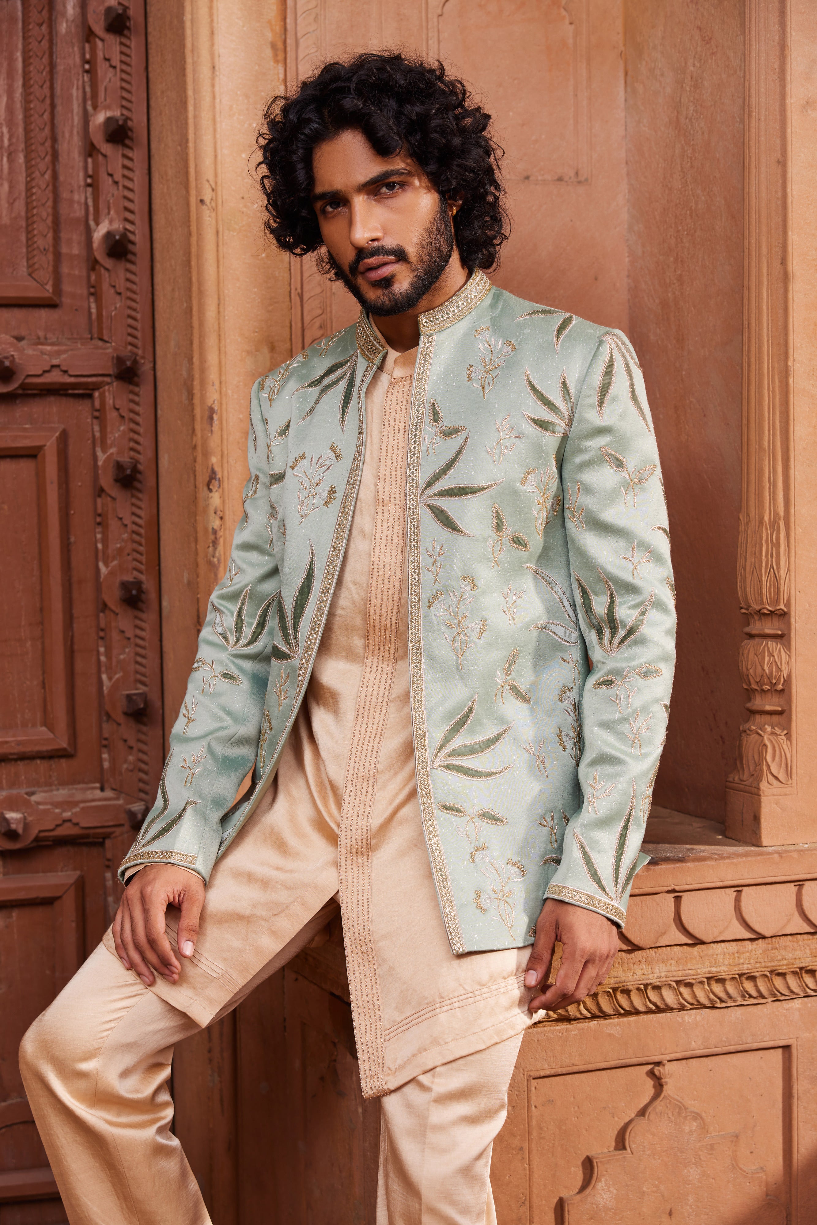 A royal jacket set, heavily embellished with tonal velvet applique work, featuring intricate dabka, zari, and cutdana embroidery. It is paired with a front-open kurta with detailed placket design and tailored pants for a regal and refined look.