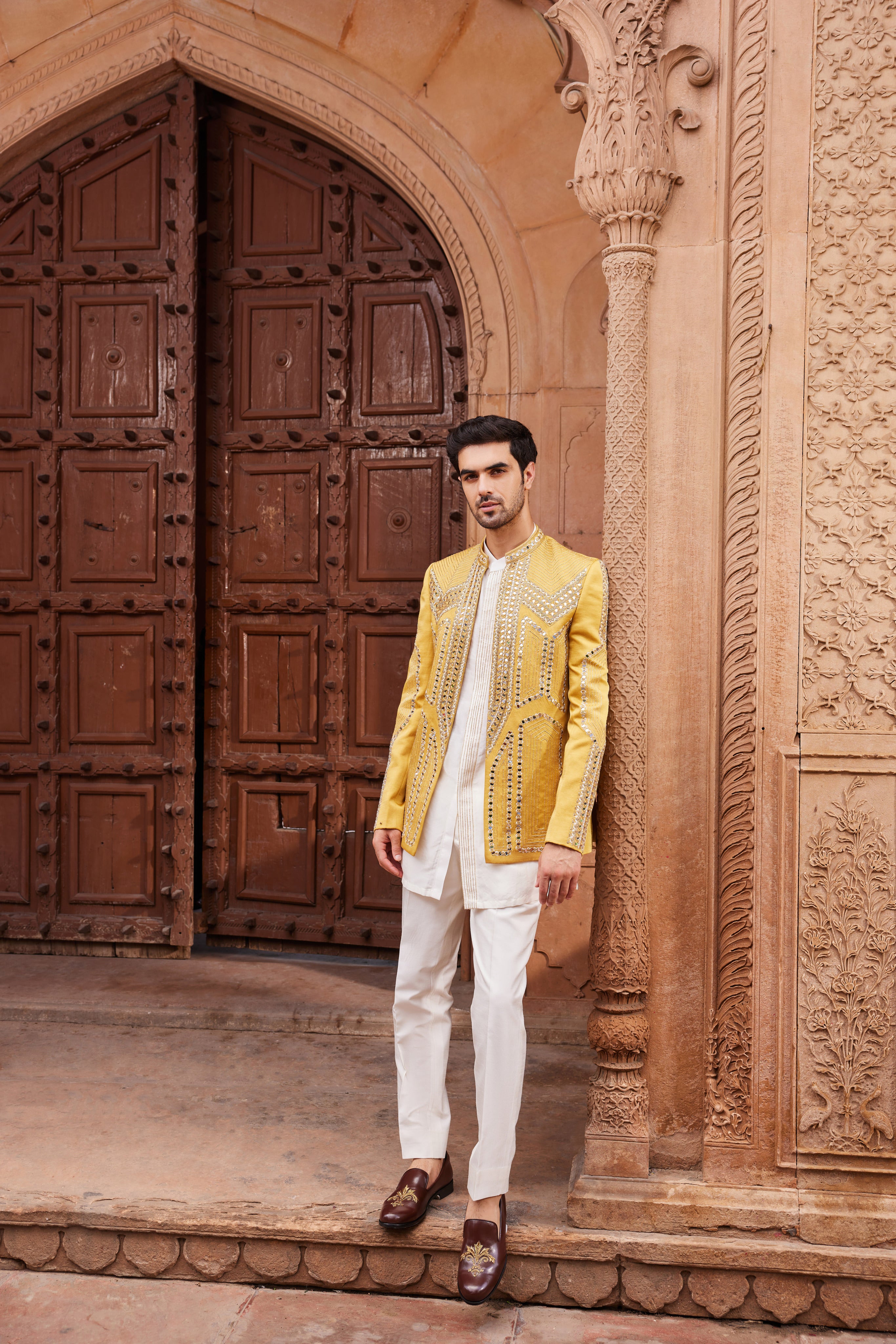 A geometric pattern jacket, heavily embellished with intricate mirror work and resham zardozi embroidery, paired with a statement front-open kurta featuring an embroidered detailed placket and matching pants.