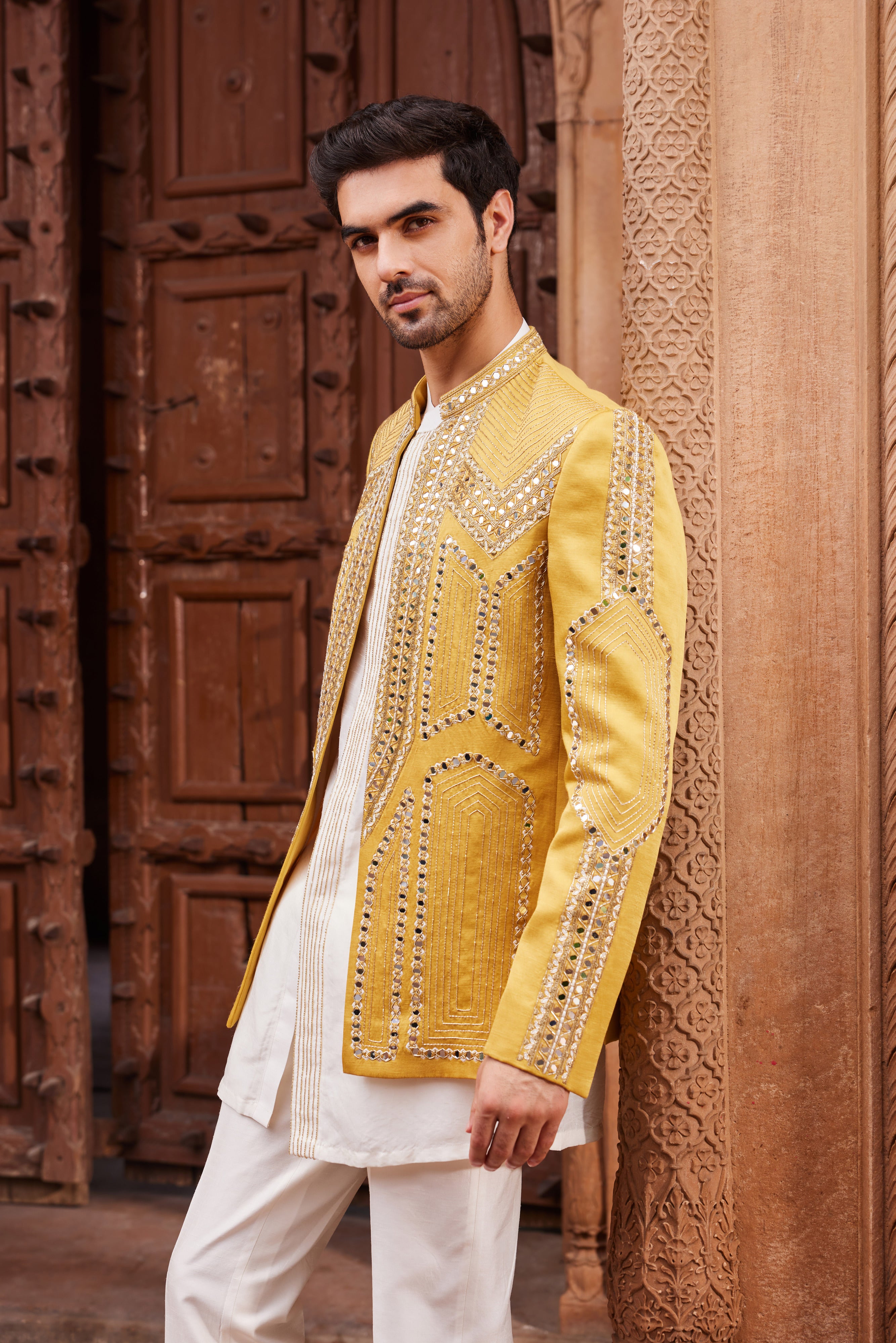 Close-up of a jacket showcasing geometric patterns adorned with mirror and resham zardozi work, paired with a front-open kurta with an embroidered placket and coordinating pants.