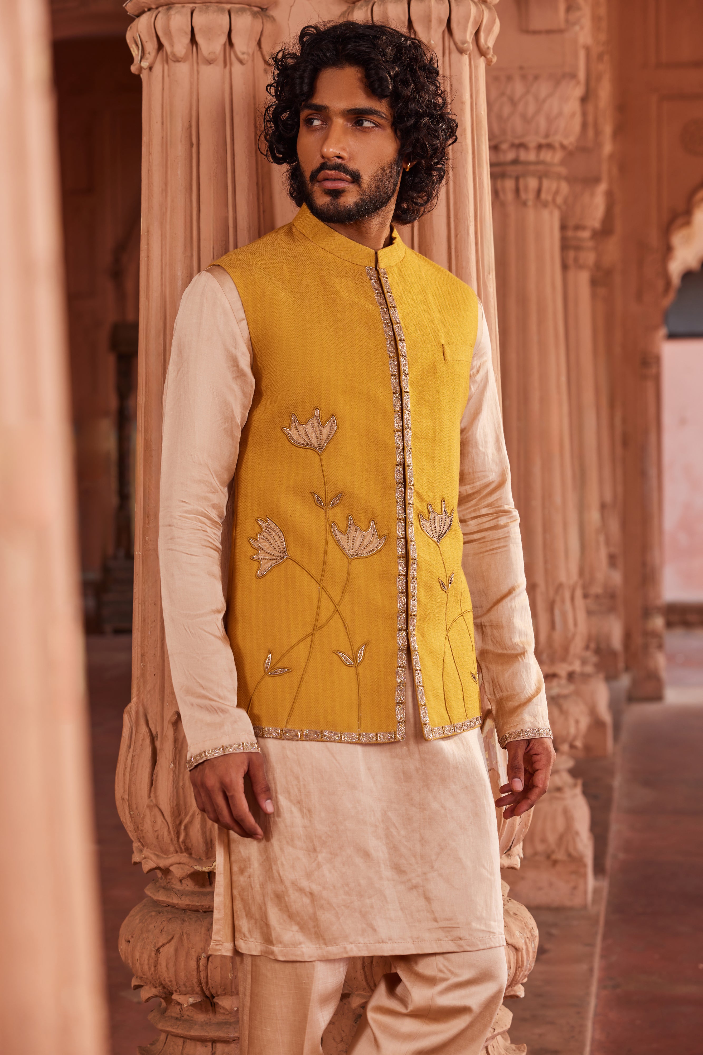 The Marigold Nehru Jacket Set includes a finely embellished jacket with tissue applique details, paired with a beige kurta and pants that feature contrast detailing