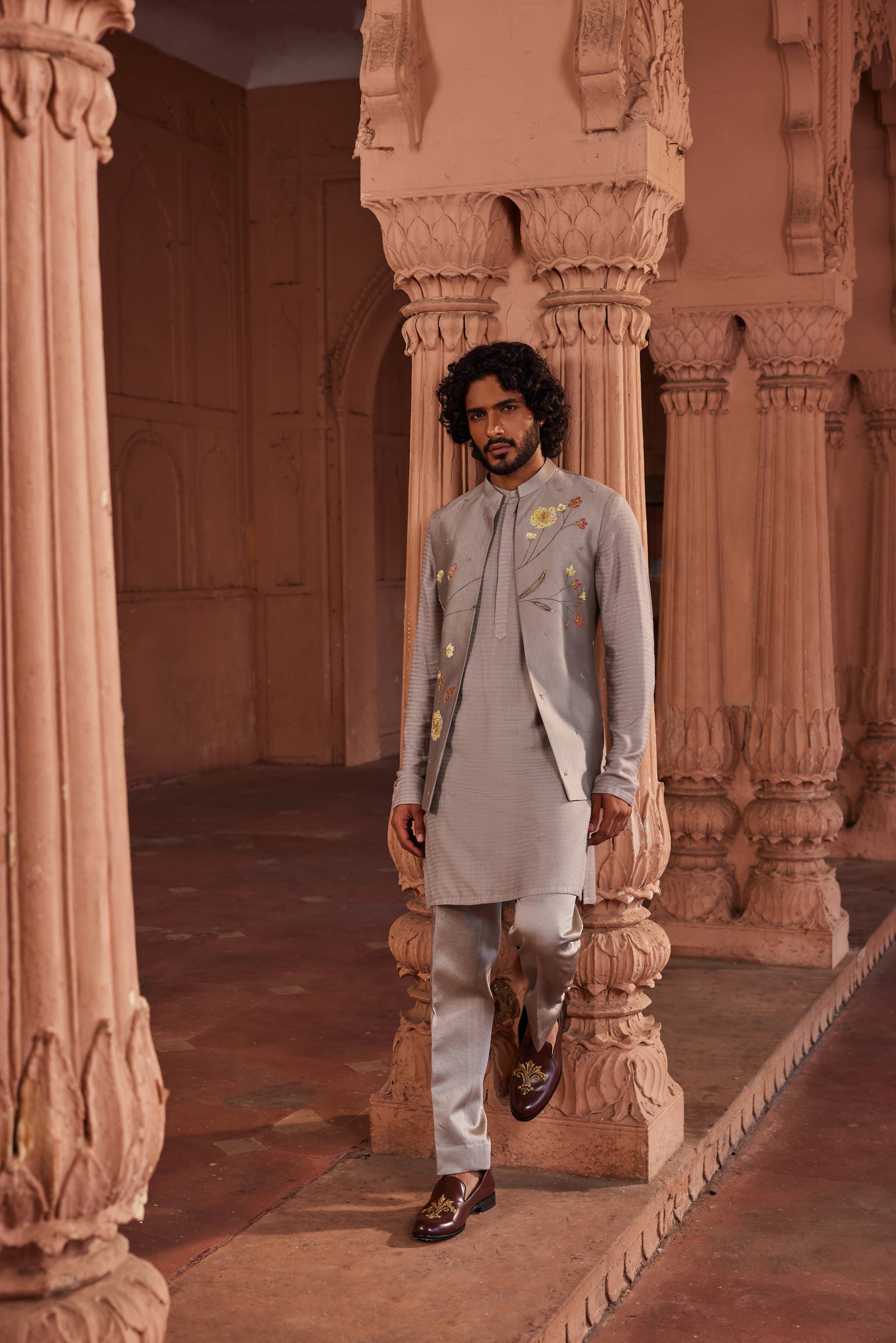 The Dusty Olive Handpaint Nehru Jacket Set features a subtle jacket adorned with colorful hand-painted floral motifs, enhanced with delicate handwork. Paired with a monotone kurta and matching pants