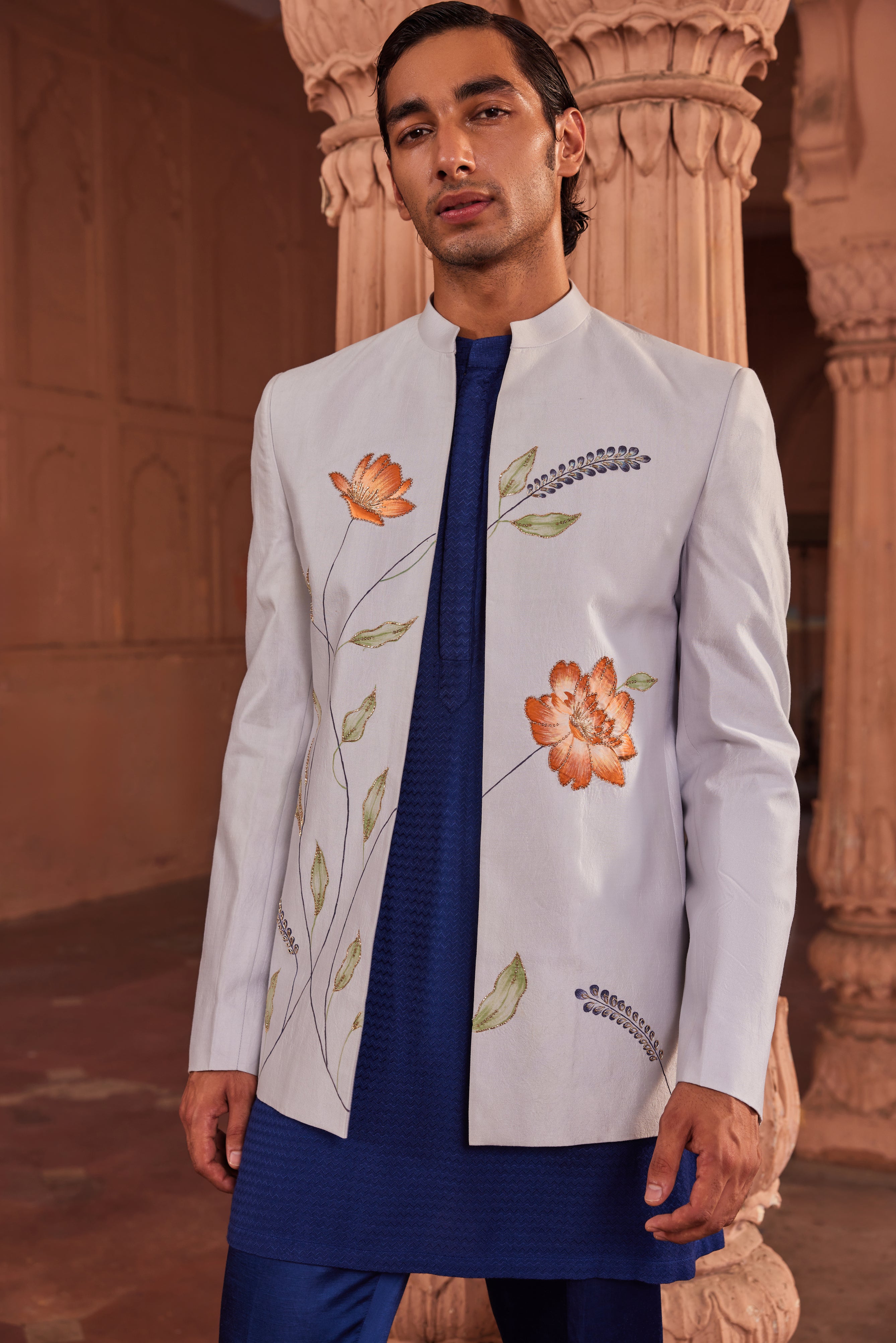 Close-up of a hand-painted jacket featuring colorful floral designs, enhanced with delicate dabka and cutdana embellishments, complemented by a contrasting kurta and pants.