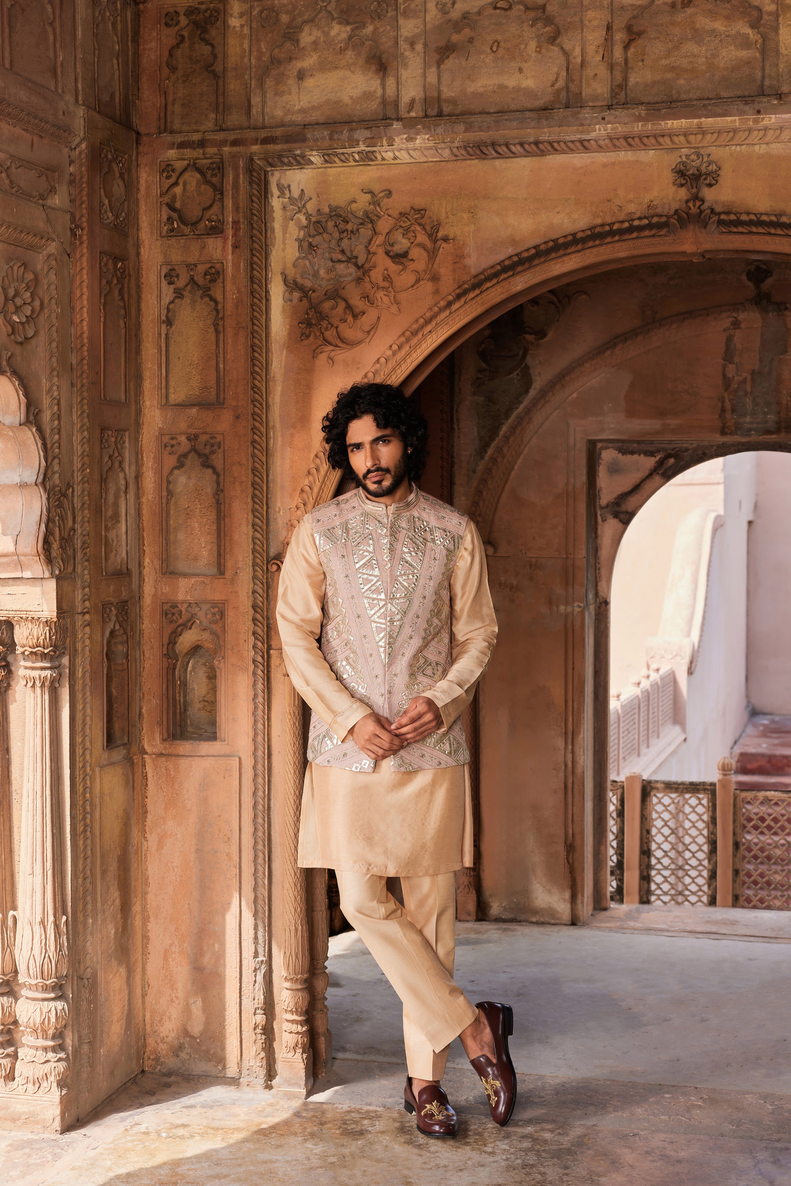 The Ibaadat Nehru Jacket Set features a geometric-patterned jacket with leather patch details, embellished with kiran dori, resham, and dabka work. Paired with a detailed kurta and matching pants