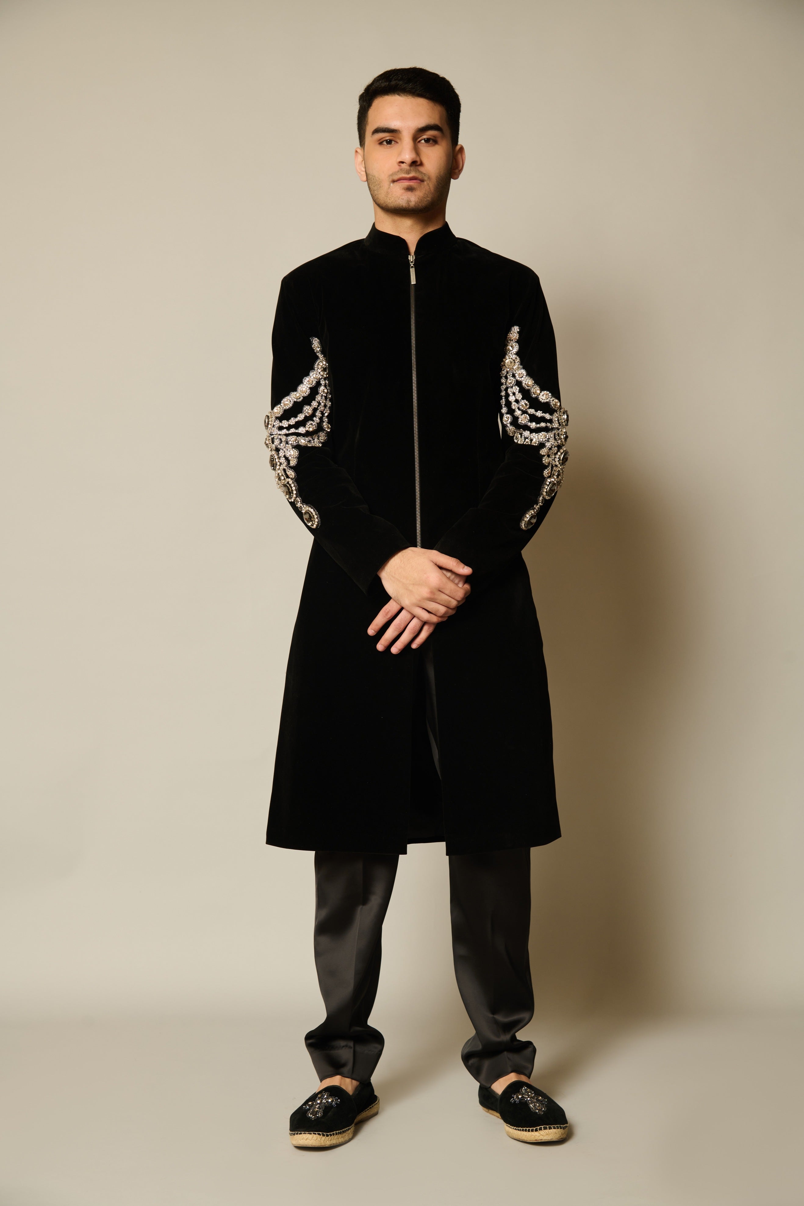 Black velvet sherwani with embroidered crystal necklace motifs on the sleeves, showcasing luxurious craftsmanship and a sleek silhouette.