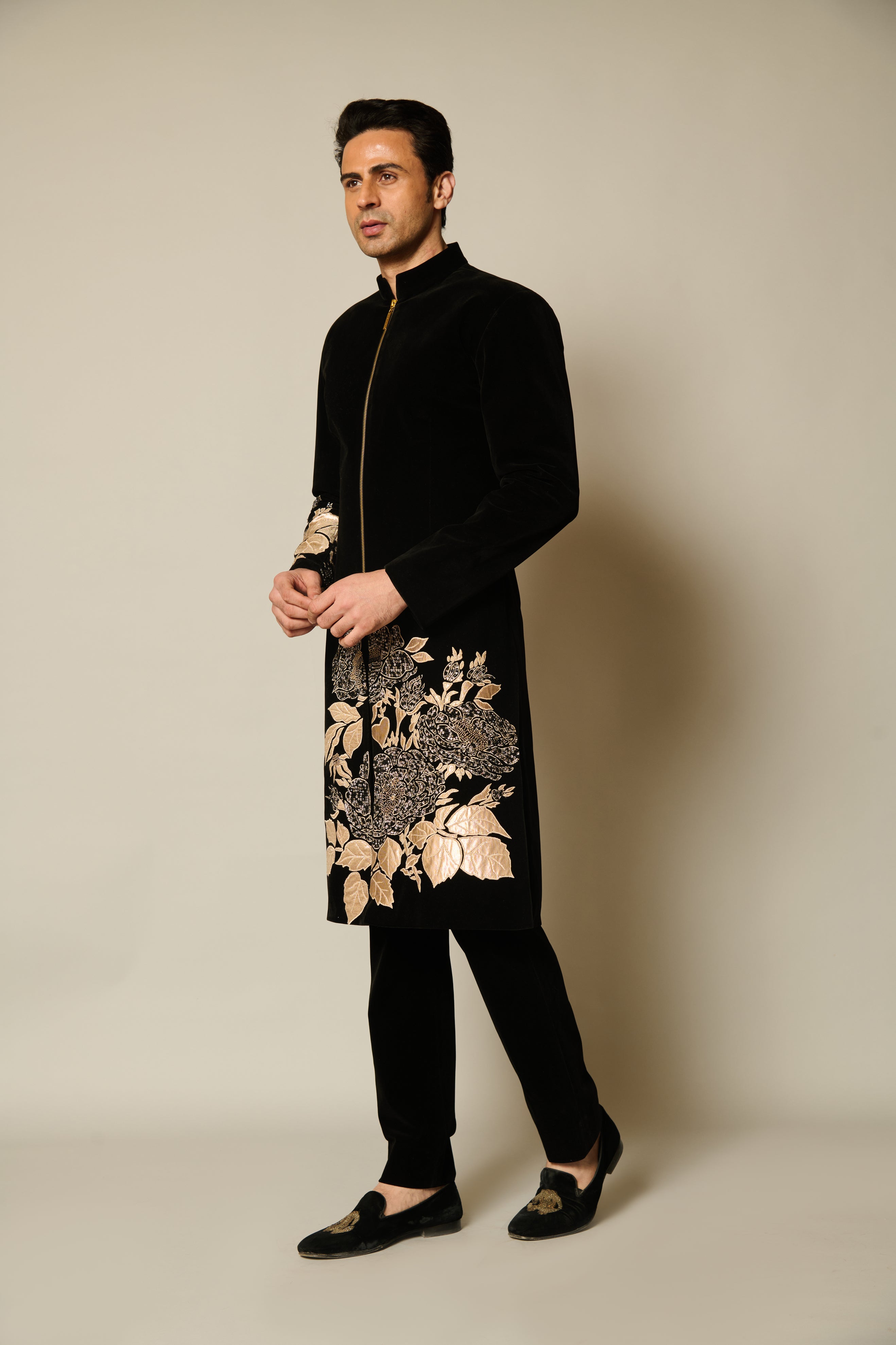  Black velvet sherwani with intricate gold floral appliqué and crystals, showcasing luxurious design and elegant craftsmanship.