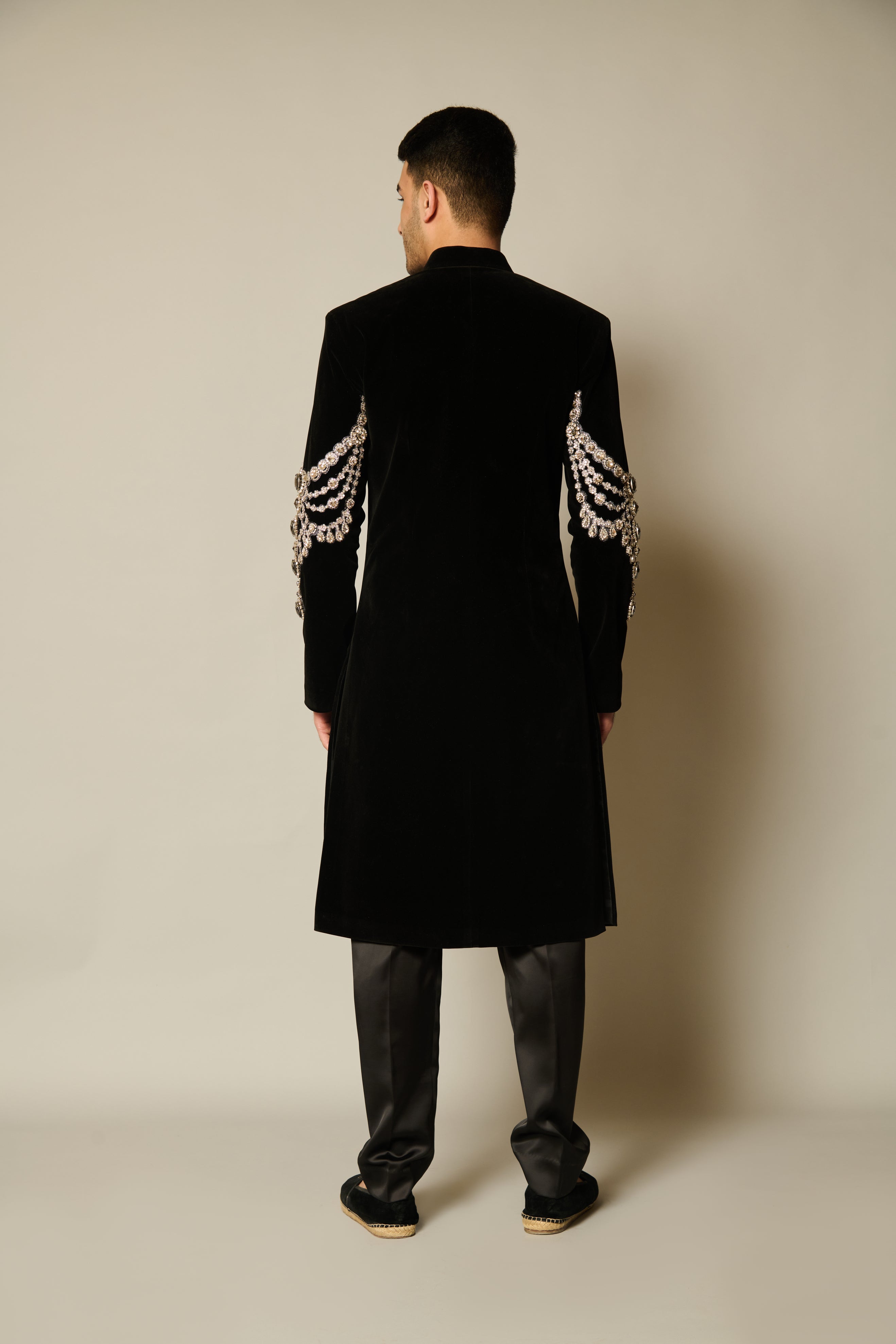 Elegant black sherwani made of rich velvet with necklace-inspired crystal embroidery on the sleeves, tailored for a sophisticated look.