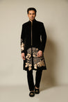 Close-up of black velvet sherwani featuring gold floral appliqué with sparkling crystals, highlighting opulent detailing.