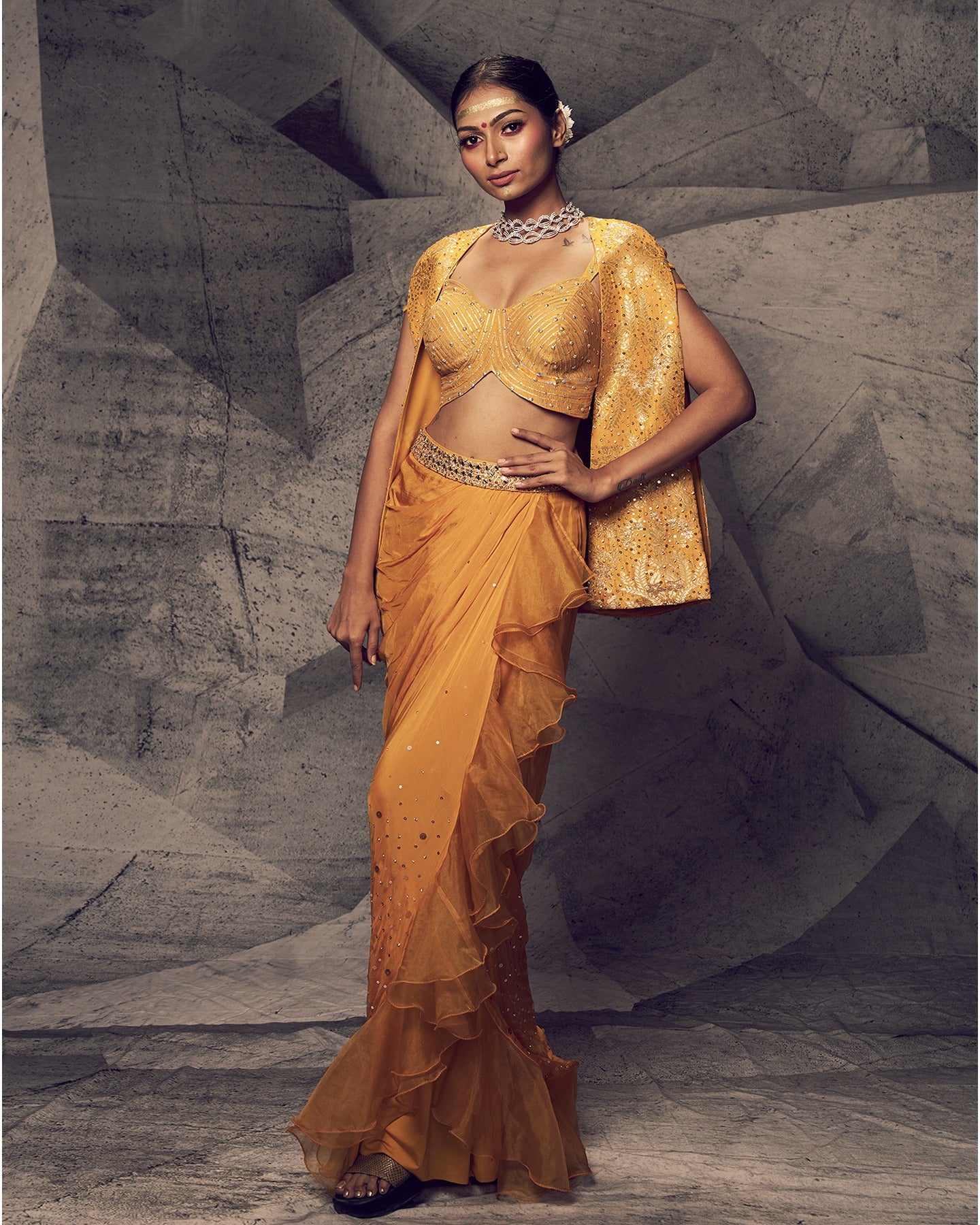 Bathed in the radiant hues of marigold, this embellished dhoti ensemble is a celebration of festive elegance. 